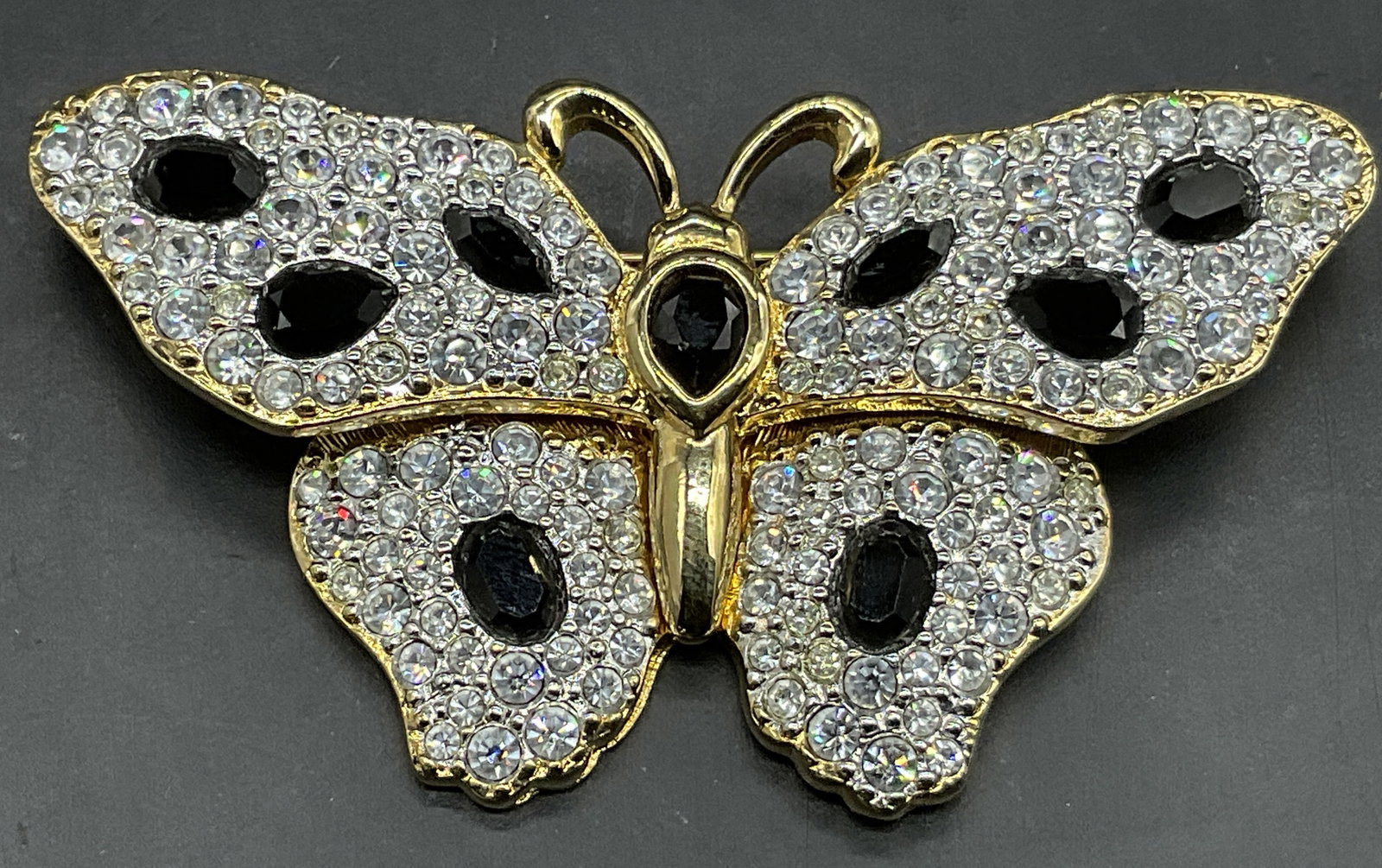 SWAROVSKI Trademarked Bejeweled Butterfly Brooch: SWAROVSKI Trademarked Bejeweled Gold Tone Metal Butterfly Brooch. Metal pin closure to underside. SWAROVSKI Swan trademark to reverse. Measures approx. 1.25L x 2.25W in. Wear consistent with age, use,