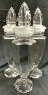 Set 3 Antique Glass Apothecary Jars W Lids: Apothecary jars appear to be antique possibly vintage. Lot includes 3 jars. Each jar is glass. Vessels are each footed. Jars each include stoppers with pointed forms. Each piece measures approx 17.5 i