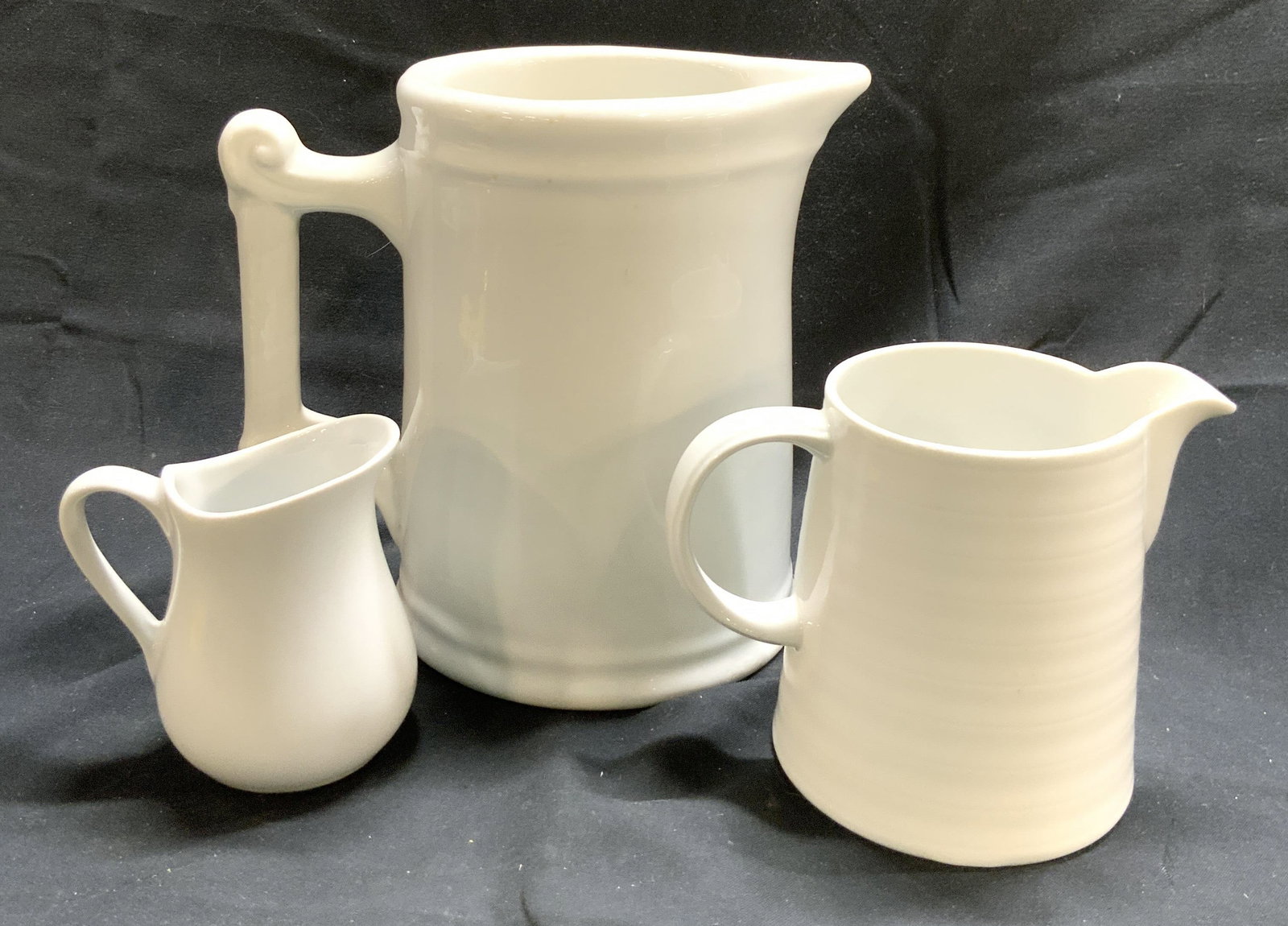 Lot3 Porcelain Pitchers CordonBleu, Crate&Barrel +: Lot includes 3 pitchers. One marked CORDON BLEU, one marked CRATE & BARREL on underside. Each pitcher is white toned and porcelain. Largest pitcher measures approximately 6.5 inches tall 7 inches deep