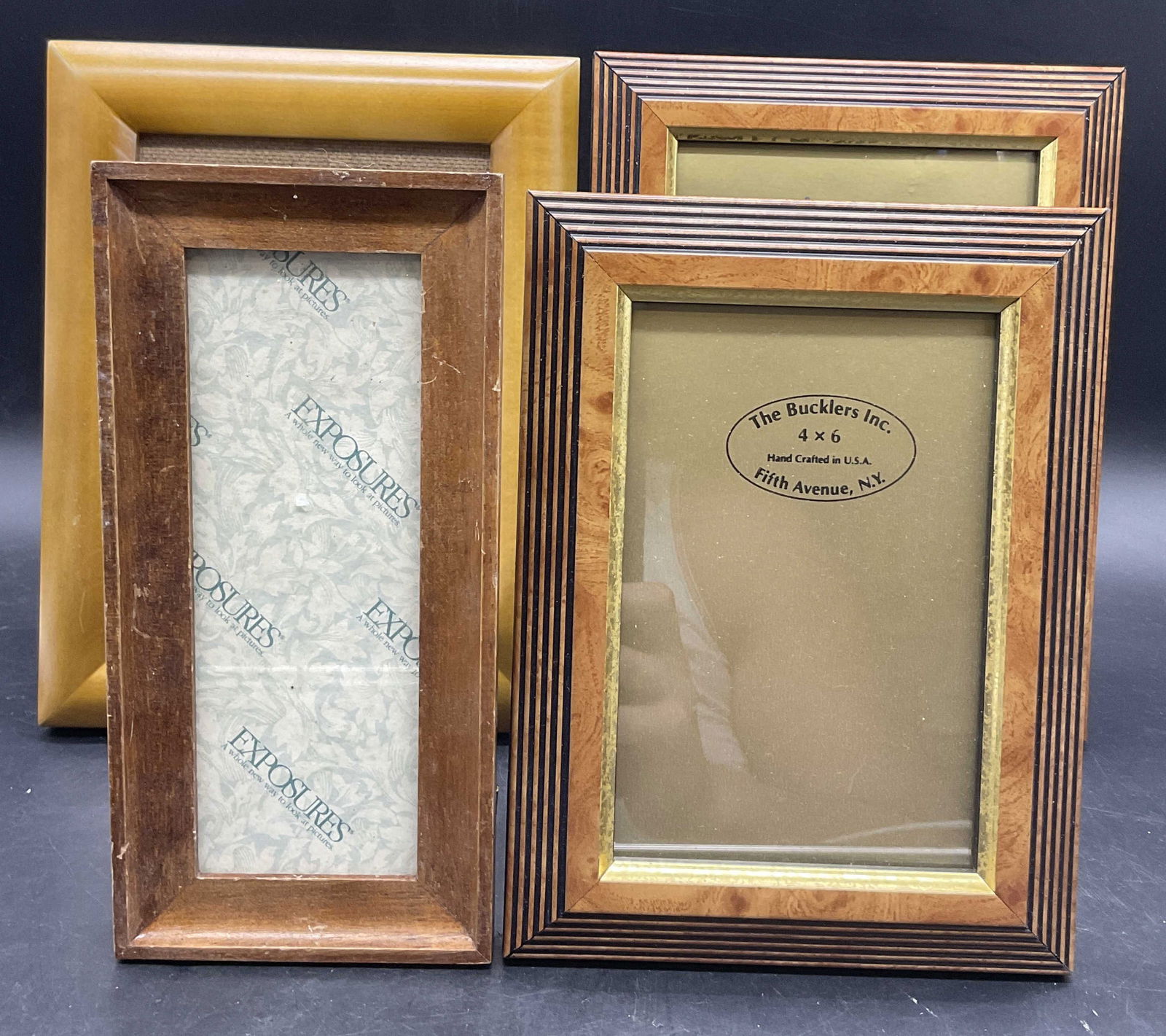 Lot 4 Vintage Wooden Picture Frames, BUCKLERS +: Two THE BUCKLERS INC. USA frames, one EXPOSURES frame, and one unbranded frame. Pieces have kickback stands. Largest measures approx. 8.75L x 6.75W in. Chipping, discoloration, and surface wear presen