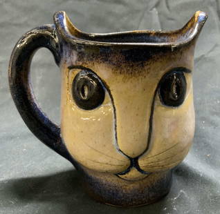 NORTH EAGLE Ceramic Cat Mug: Underside is inscribed NORTH EAGLE. Mug is in the form of a cat head. Piece is tan, slate and dark blue toned. Mug has 2 pointed edges as ear forms. Mug measures approximately 4.5 inches tall 4.75 inc