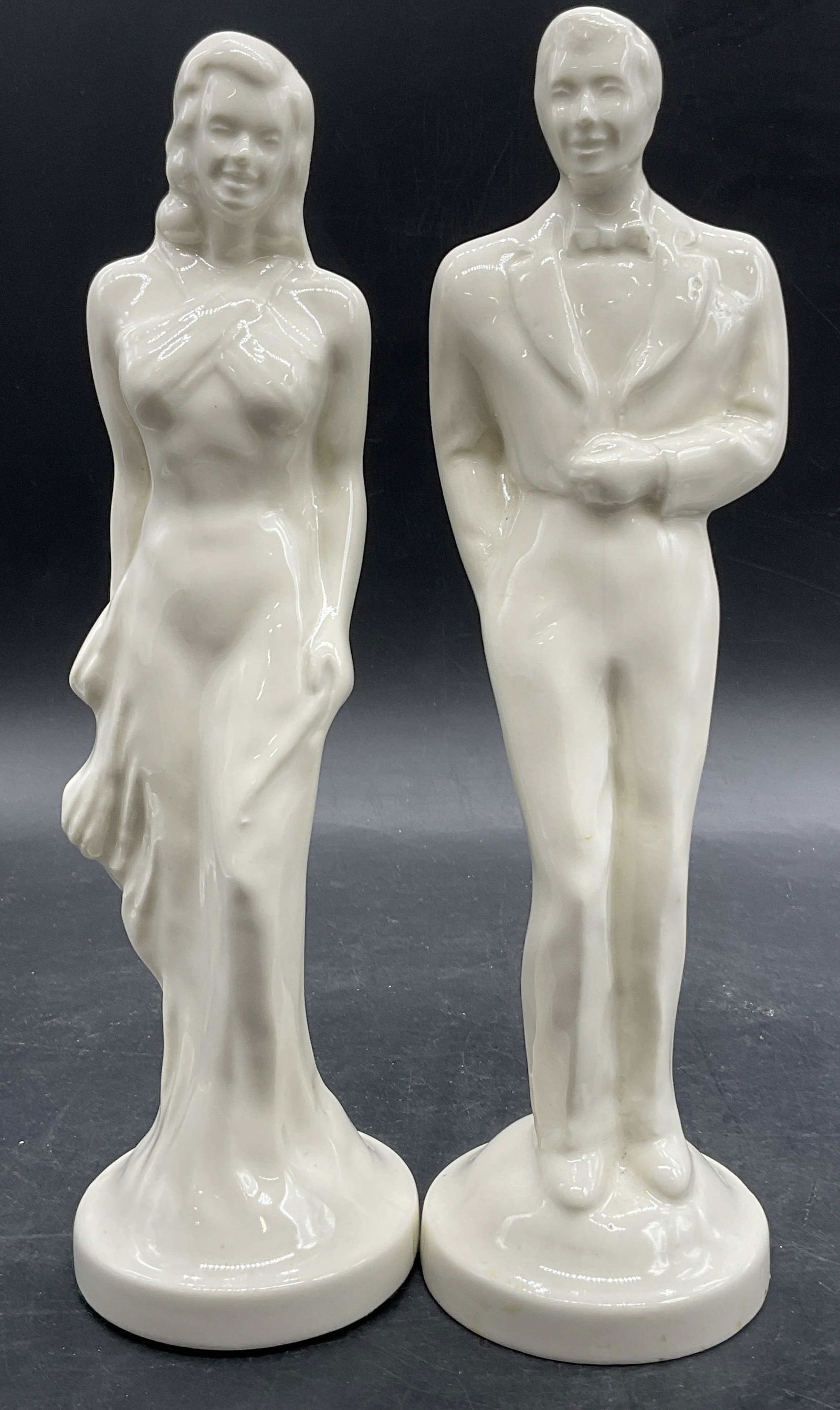 2 Vintage White Ceramic Man & Woman Figurals: Vintage White Ceramic Man & Woman Figurals. Both the man and the woman wear formal attire. Woman measures approx. 10H x 3W in. Felt to one underside. Pitting, losses to glaze, surface wear, and residu