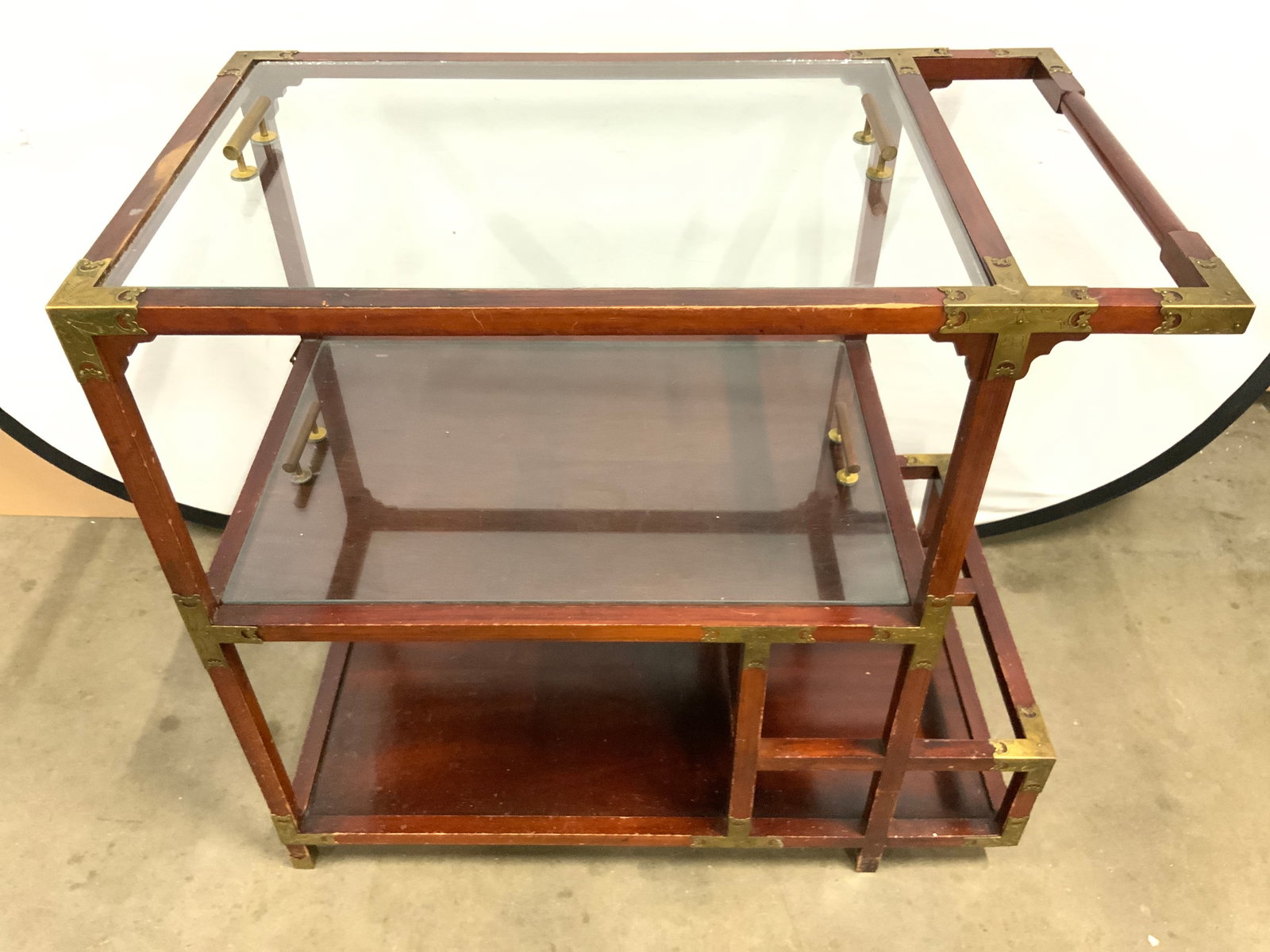 FURNITURE CLASSICS LTD Vtg Wooden Bar Stand: Tag reads FURNITURE CLASSICS LTD. Bar stand is vintage. Piece is brown toned and wooden. Bar stand includes 2 glass trays with brass handles. Piece has gilt metal adornments. Measures approx 32.5 inch