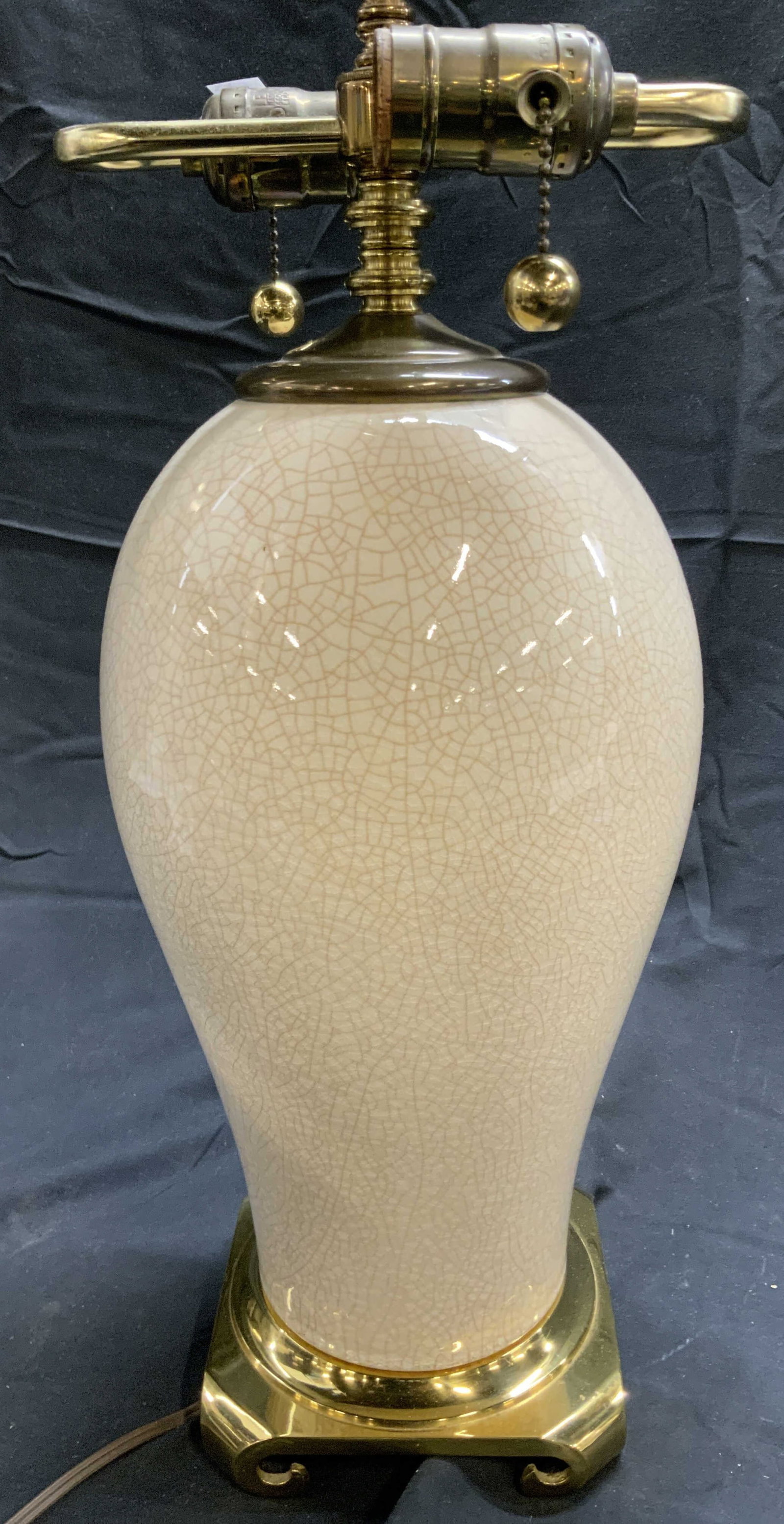 CRESCENT BRASS Mfg Base Porcelain Tbl Lamp: Underside is inscribed CRESCENT BRASS MFG. Lamp is cream toned, appears to be porcelain. Lamp has 2 bulb sockets each with dangling pull switches. Base is footed. Lamp includes harp and finial. Measur