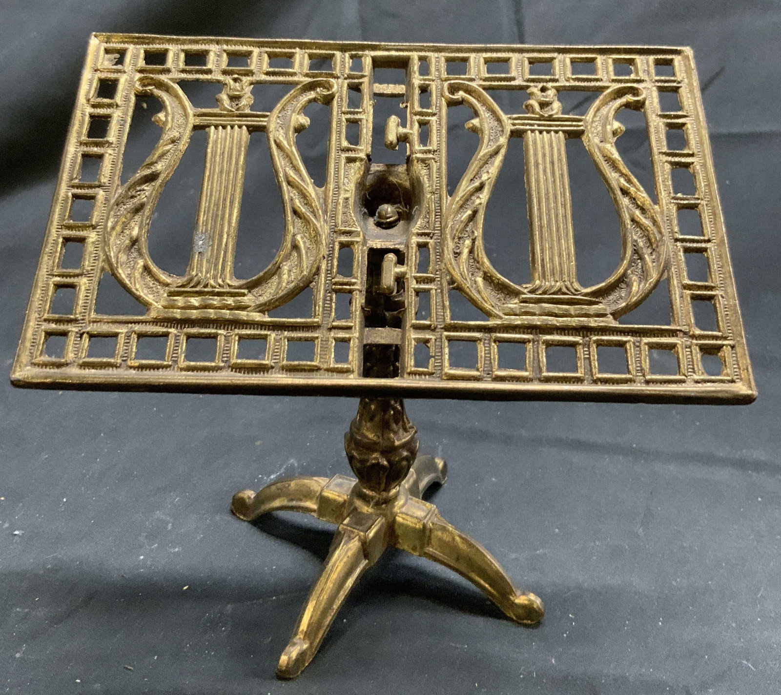 Vintage Brass Miniature Music Stand: Music stand is miniature in size. Piece is gold toned and brass. Stand has quad pod foot. Top of piece has lyre detail along with pierced geometric detail. Music stand is vintage. Piece measures appro