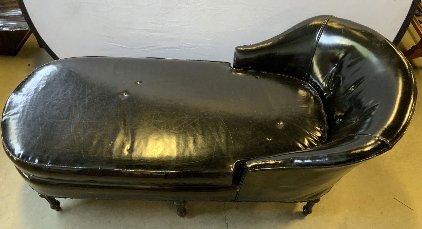 Vintage Patent Leather Tufted Fainting Couch Blk: Fainting couch is upholstered in black toned patent leather. Backrest is tufted and has barrel form. Fainting couch has 6 black toned carved wooden legs. Edges of upholstery have nailhead detail. Vint
