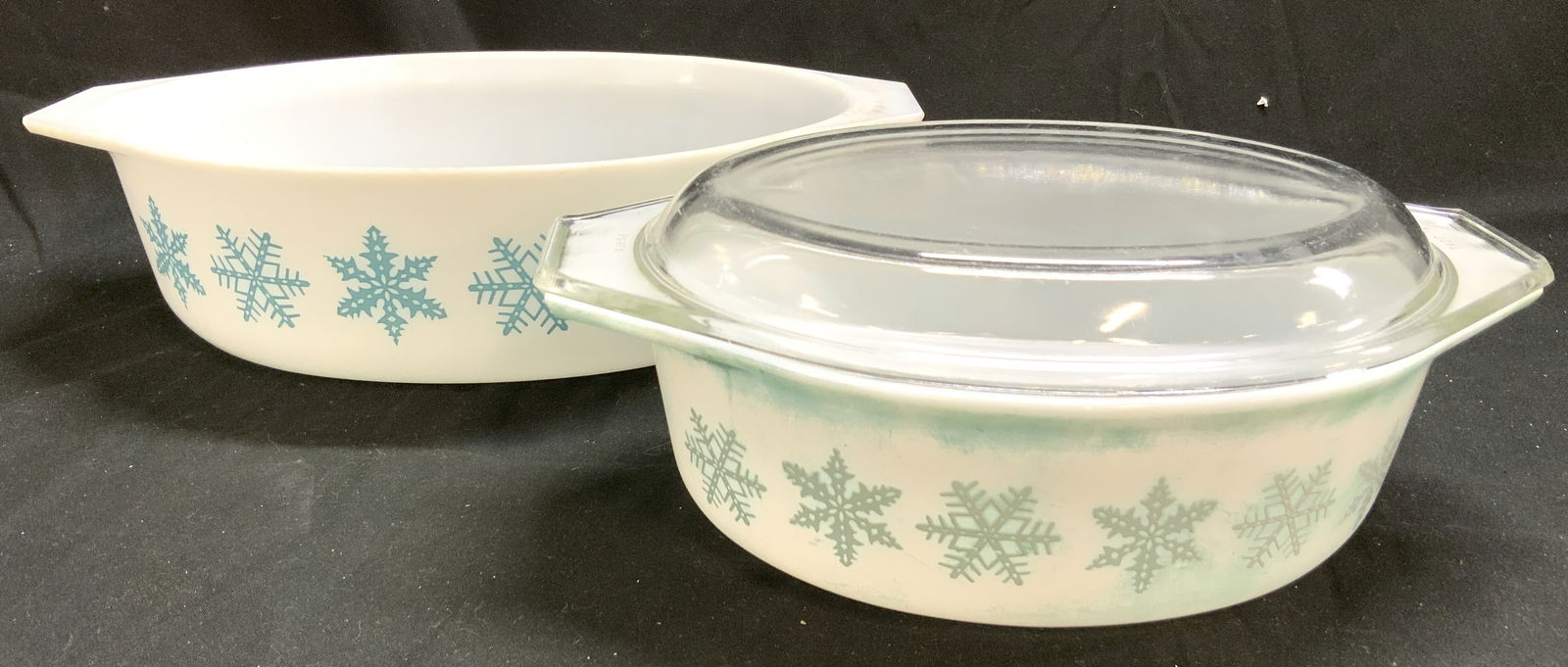 PYREX Lot 2 Snowflake Serving Dishes: Undersides of each read PYREX. Lot includes 2 serving dishes. One dish includes clear lid. Each dish is white toned with snowflake detail. Sides of each dish have handles. Largest dish measures approx
