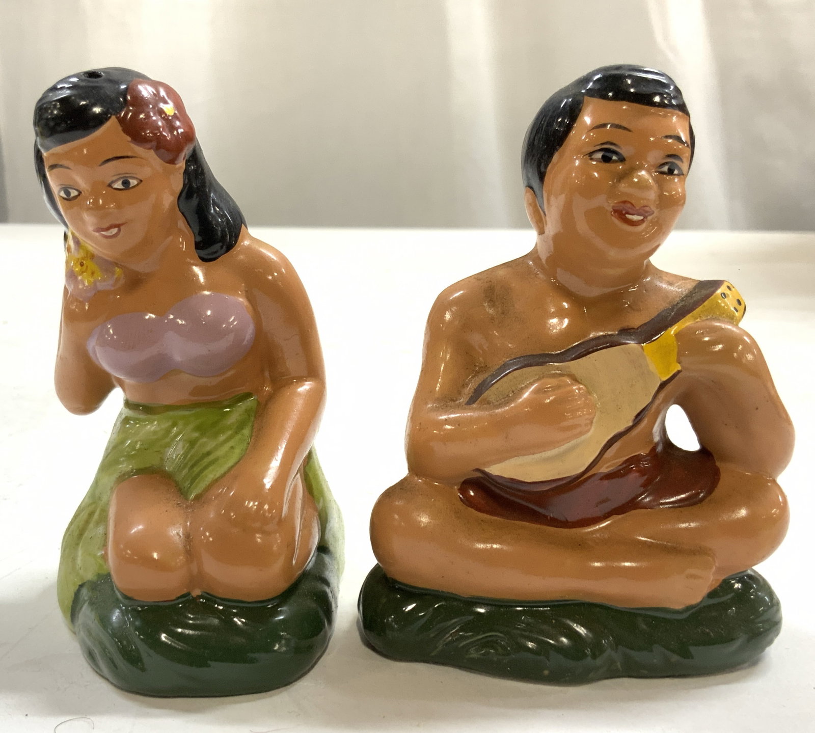 Vtg H Painted Hawaiian Male & Female S&P Shakers: Lot include 1 salt & 1 pepper shaker. Shakers include 1 seated male figure playing ukulele, & 1 kneeling female figure in leaf skirt. Each piece is porcelain & appears to be hand painted. Male figure 