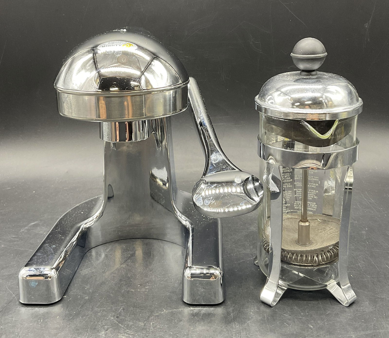 Lot 2 Silver Tone Metal Juice Press & Coffee Press: Lot of 2 Silver Tone Metal Juice Press & Coffee Press. The juice press has a sticker which reads MIGHTY OJ and the coffee press is marked Bodum. Coffee press is crafted from plastic, metal, and glass