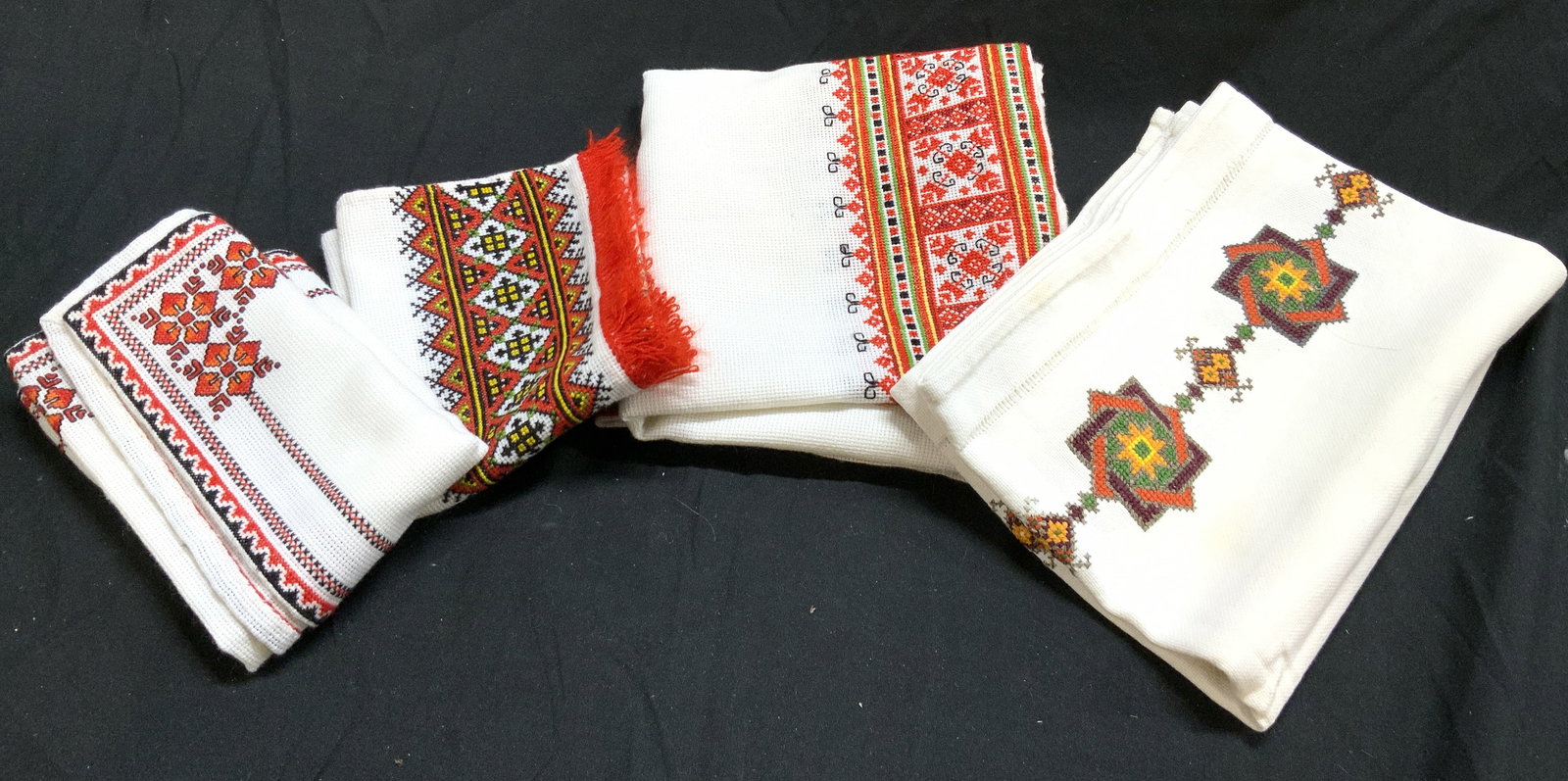 Lot 4 Ukrainian Rushnyk Towels & Table Linen: Lot includes 3 Ukrainian Rushnyk towels & 1 table linen. Each Rushnyk has red, white and black toned geometric patterned detail. One piece has red toned fringes. Table linen has multi toned needlepoin