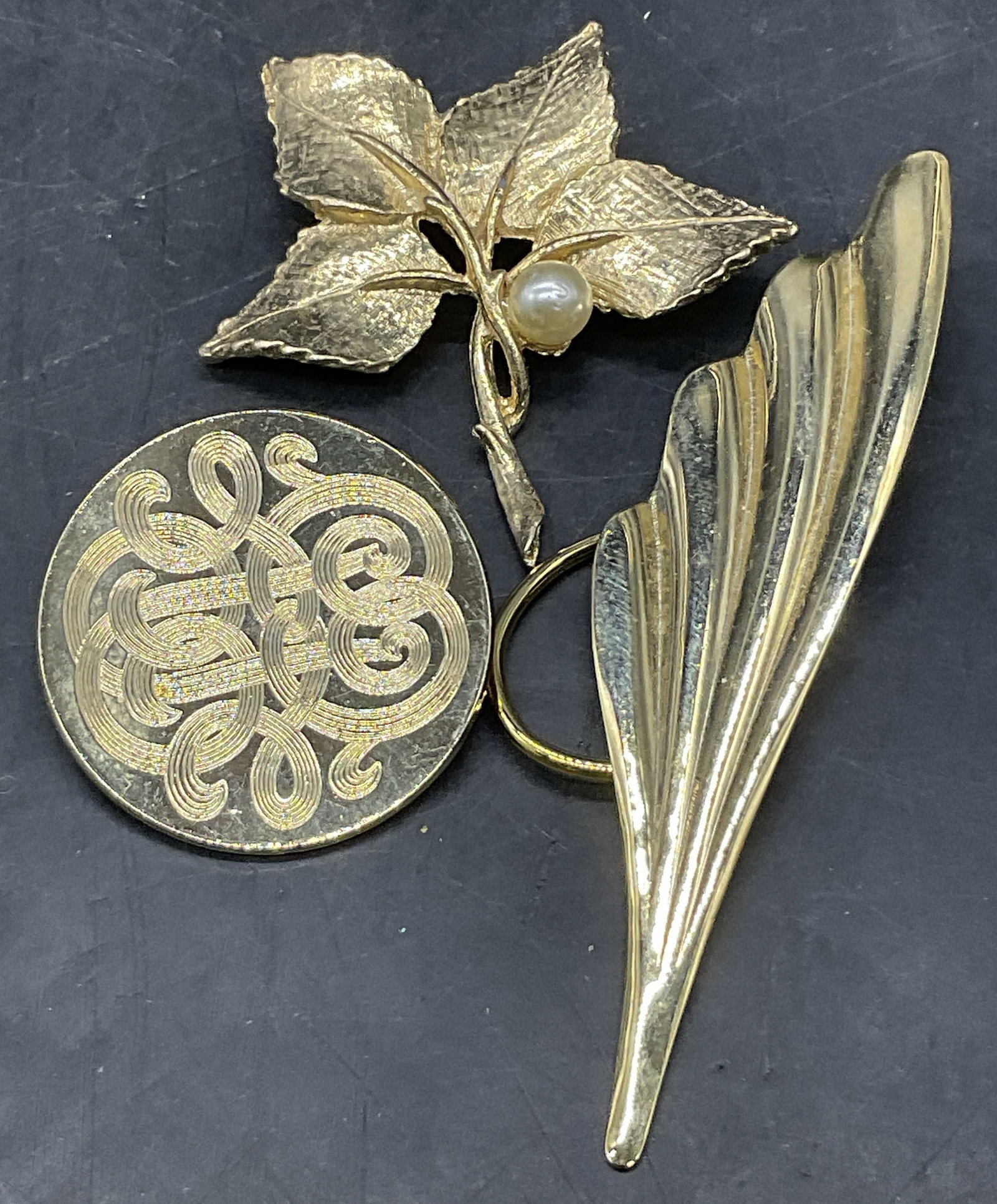 Lot 3 Vintage Gold Tn Metal Sweater Clips & Brooch: Lot of 3 Vintage Gold Tone Metal Sweater Clips & Brooch. A round sweater clip with an etched design, an abstract leaf form sweater clip, and a leaf motif brooch with a pearlescent bead. Closures to th
