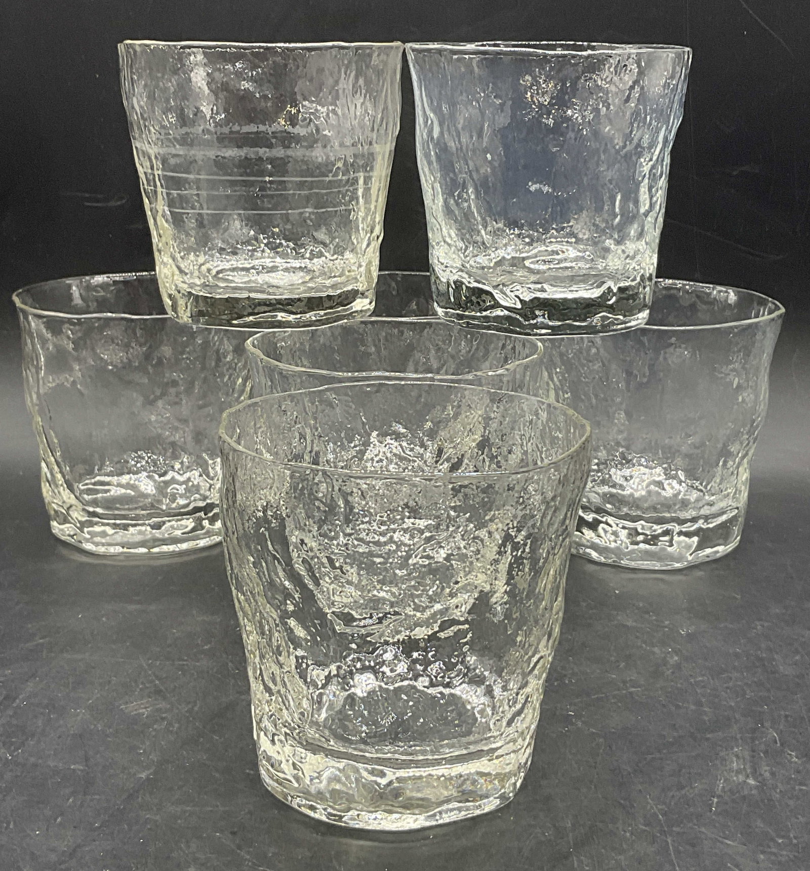 Set 7 Clear Textured Glass Cups: Set of Seven Clear Textured Glass Cups. Organic irregular forms. Measures approx. 3.5H x 3.5W in. Bubbles to glass. Discoloration and residue present. Surface wear consistent with age, use, and exposu