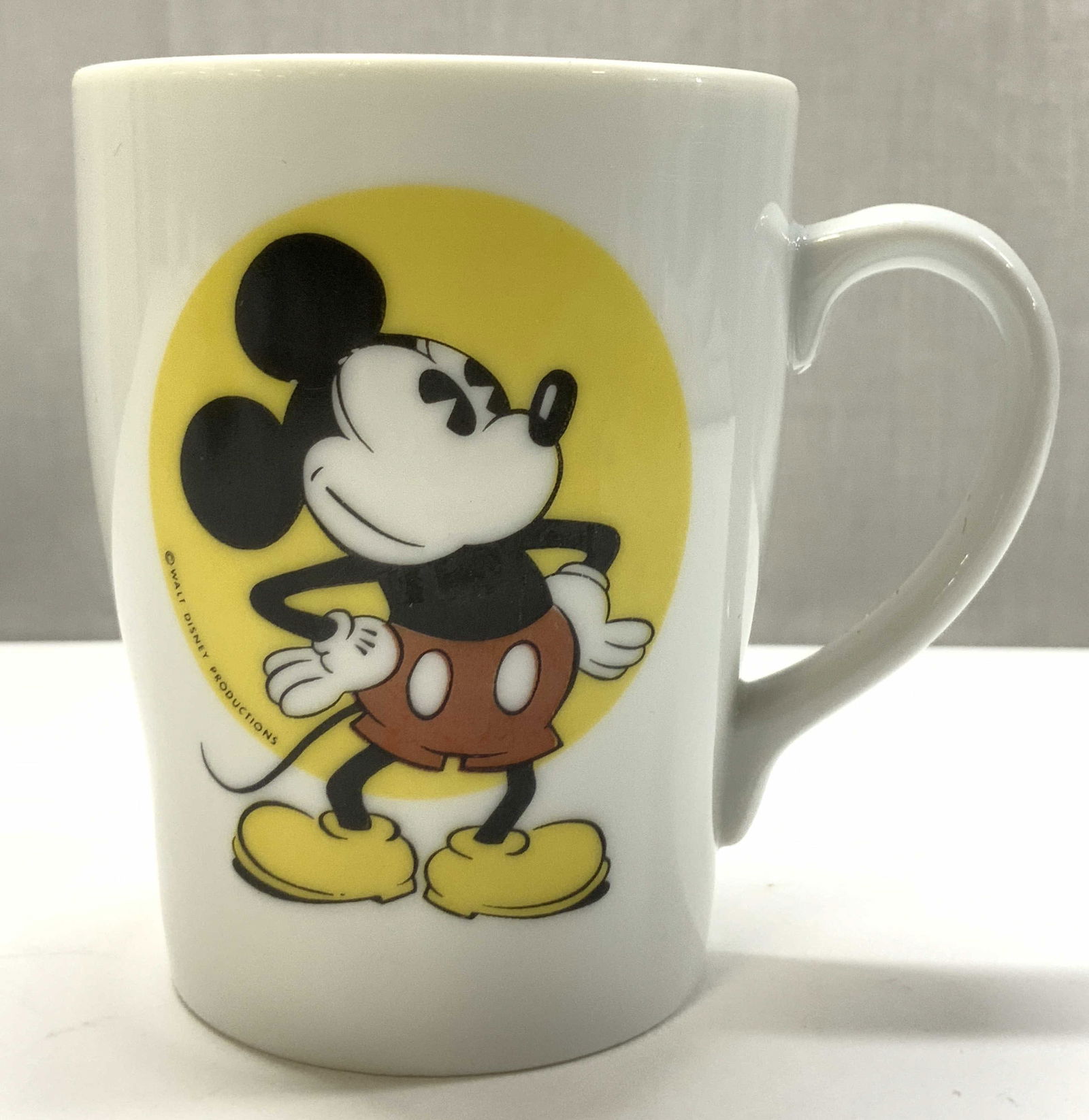 WALT DISNEY Mickey Mouse Coffee Cup JAPAN: WALT DISNEY Mickey Mouse Coffee Cup JAPAN Coffee cup has an illustration of Mickey Mouse on a yellow circular background. Signed & marked on underside of cup. Reads WALT DISNEY, JAPAN. Surface wear co