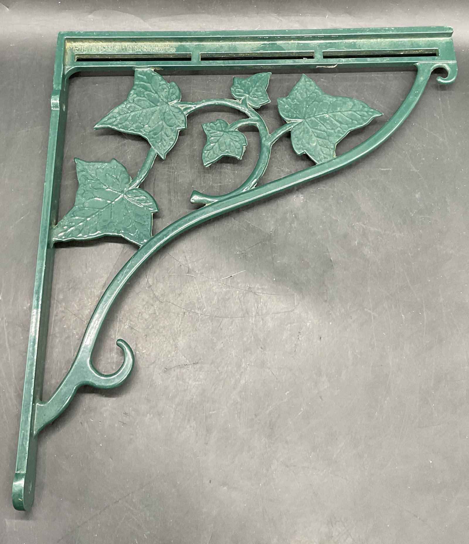 MENAGERIE WORKS USA Green Metal Wall Hook USA: MENAGERIE WORKS USA Green Metal Vine Motif Wall Hook. Top reads MENAGERIE WORKS PORTLAND OREGON USA. Measures approx. 13L x 12W in. Sticker residue, surface wear, and discoloration present. home decor