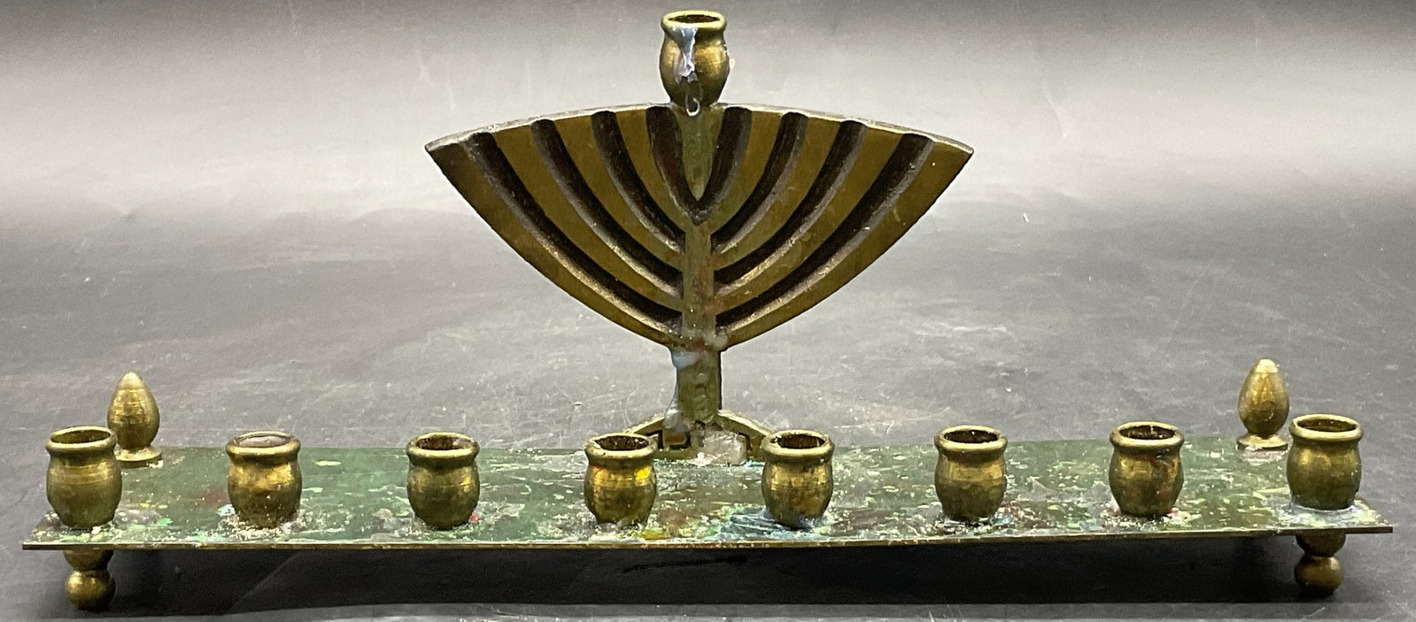 Vintage Brass & Metal Judaica Hanukkah Menorah: Vintage Brass & Metal Judaica Hanukkah Menorah. Hebrew writing to obverse. Measures approx. 3.5H x 8.5W in. Residue, loose pieces, losses to finish, and discoloration present. home decor, home accents