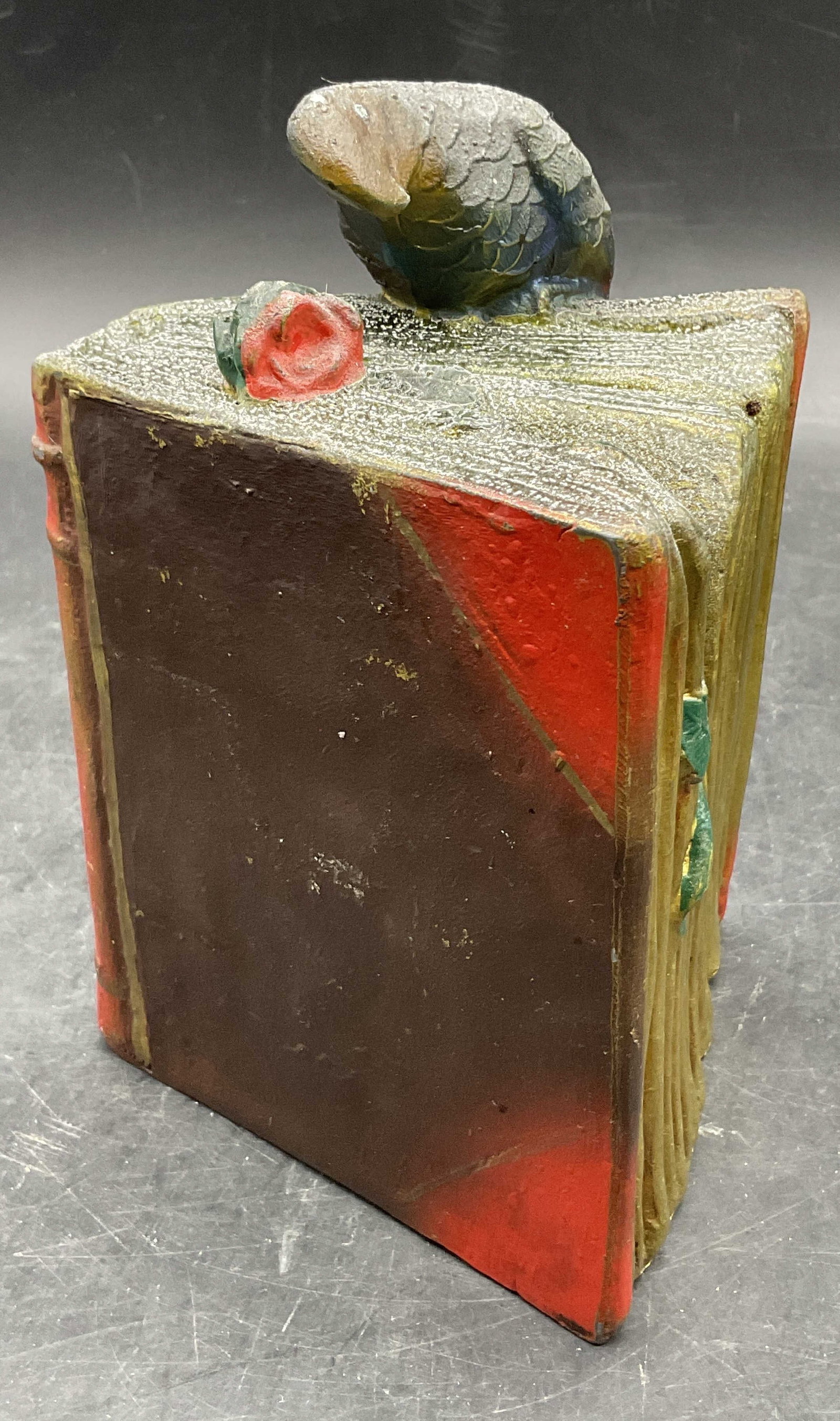 Vintage Painted Metal Parrot Atop Book Figural: Vintage Painted Metal Parrot Atop Book Figural / Bookend. Measures approx. 6H x 4W in. Measured at widest point. Weighty. Discoloration, residue, pitting to the metal, and surface wear present. home d