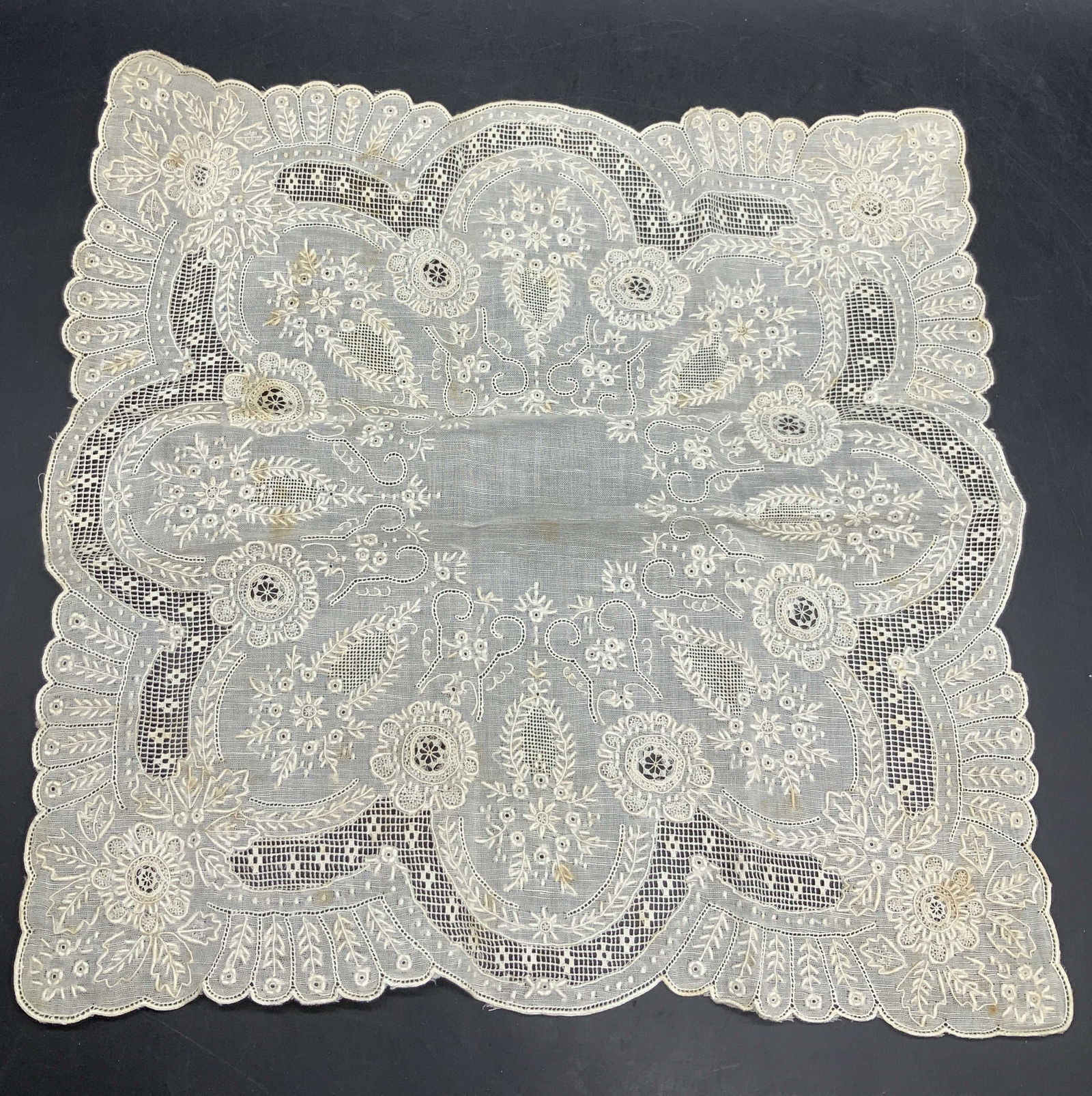Vintage Handmade Embroidered Linen Handkerchief: Vintage Handmade Embroidered Linen Handkerchief. Floral and foliage motif to the piece. Pierced fabric details throughout the design. Scalloped edge. Measures approx. 11.25L x 11.25W in. Discoloration