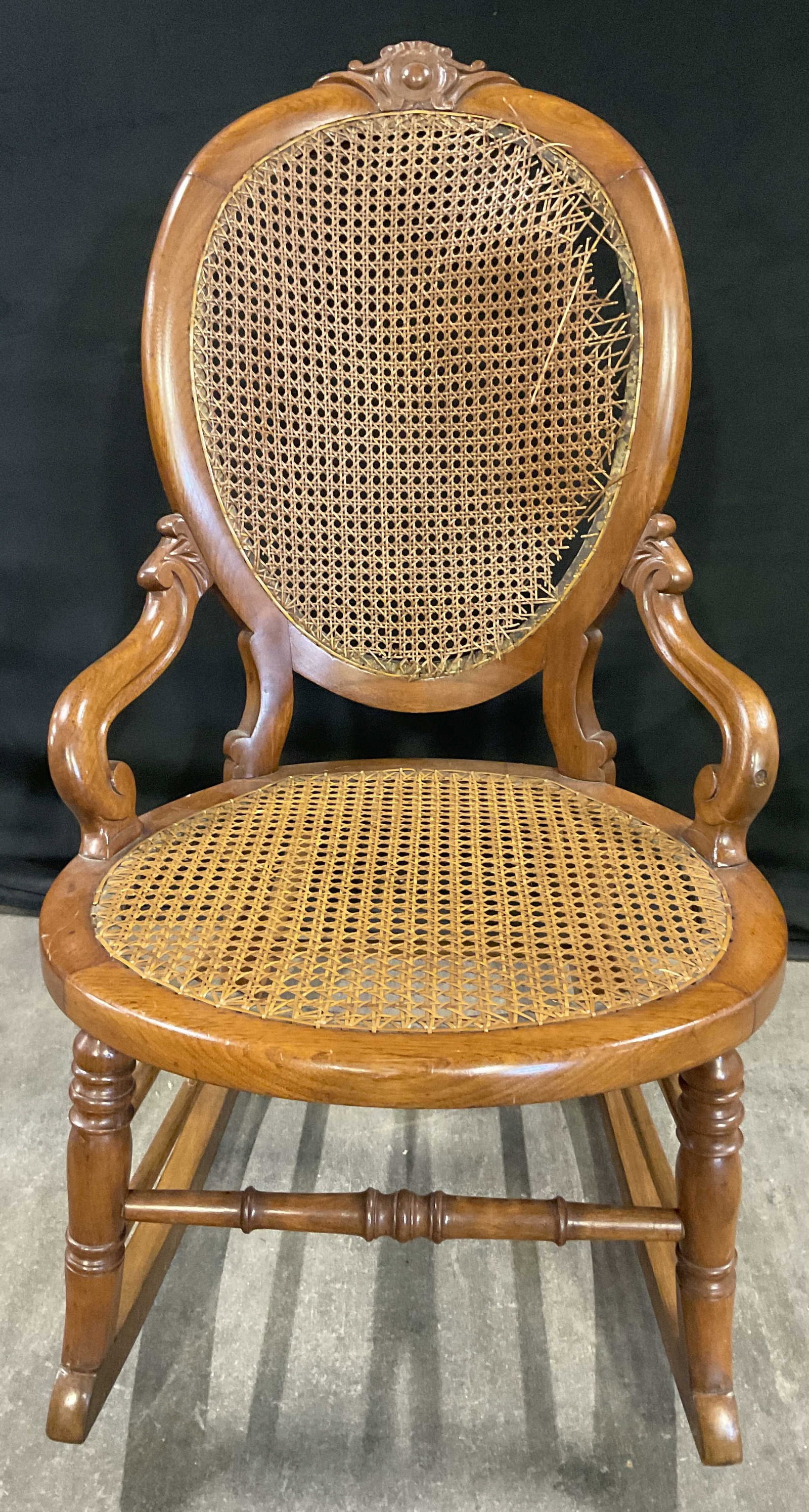Vintage Caned Wooden Rocking Chair: Vintage Caned Wooden Rocking Chair. Caned seat and backing. Carved wood details. Scrolled arms to the piece. Measures approx. 29D x 34H x 20W in. Depth measured at rocking legs. Losses to the cane, su