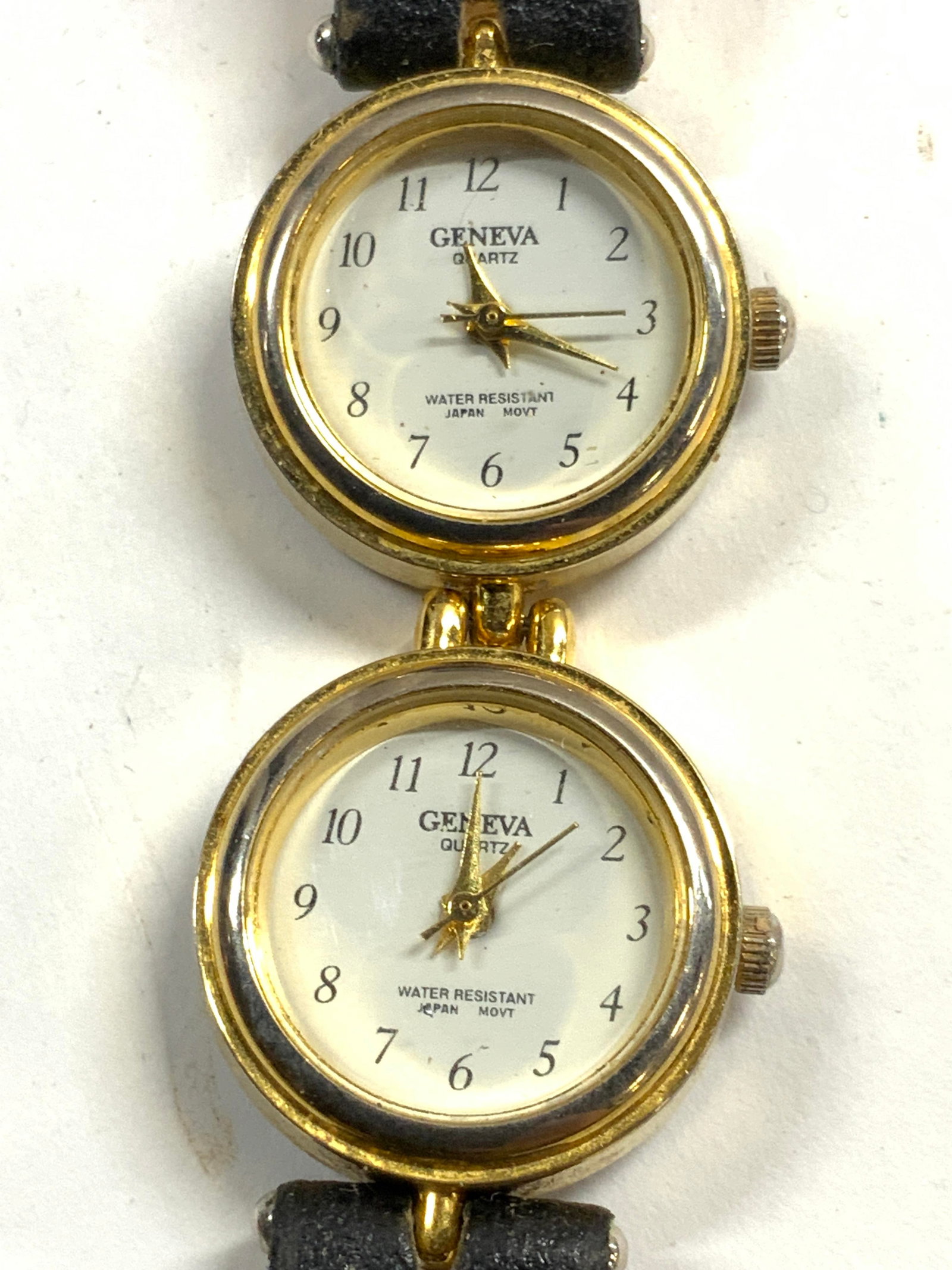 GENEVA Womens Double Face Wristwatch: Watch has 2 faces. Each watch face reads Geneva. Watch has black toned band, white faces with black toned hands and numbers, gilt metal frames. Watch measures approximately 8.75 inches long 1 inch wid