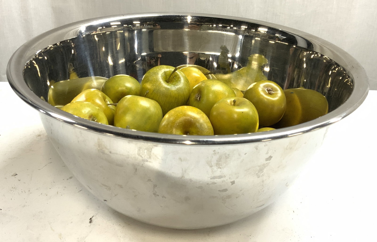 AMCO Stainless Bowl W 20 Faux Crab Apples: Underside of bowl reads AMCO. Lot includes 1 stainless metal bowl and 20 faux crab apples. Bowl is silver toned. Outer rim has lip. Bowl measures approximately 12 inches diameter 5.5 inches tall. Bowl