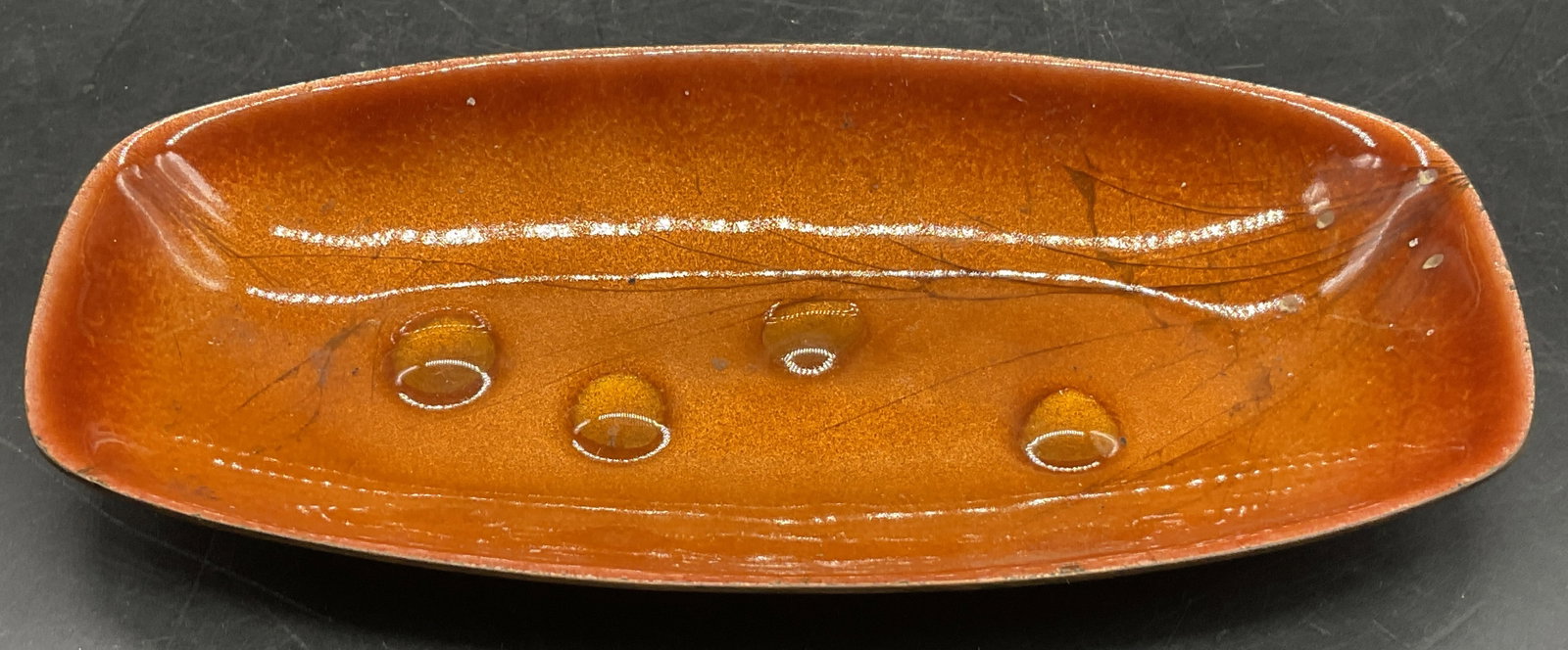 BOVANO Handcrafted Enamel Trinket Dish, Conn: BOVANO Handcrafted Enamel Trinket Dish. Oranges hued enamel obverse and black base. Underside sticker reads HANDCRAFTED BY BOVANO, CHESHIRE CONN. Measures approx. 5.75W x .75H in. Measured at widest p
