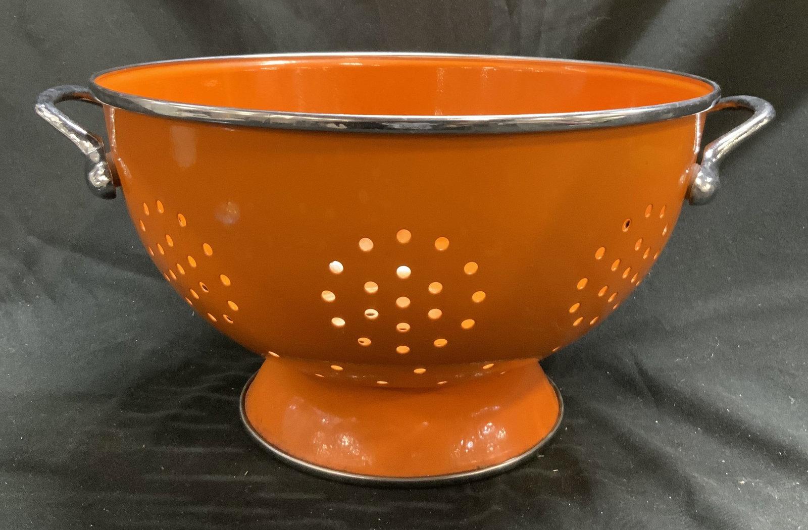 Vintage Orange Metal & Enamel Colander W Handles: Colander is orange toned. Piece is metal and enamel. Colander has silver toned rim and handles. Piece is footed. Measures approximately 6 inches tall 12 inches wide 10.25 inches deep. Colander, metal 