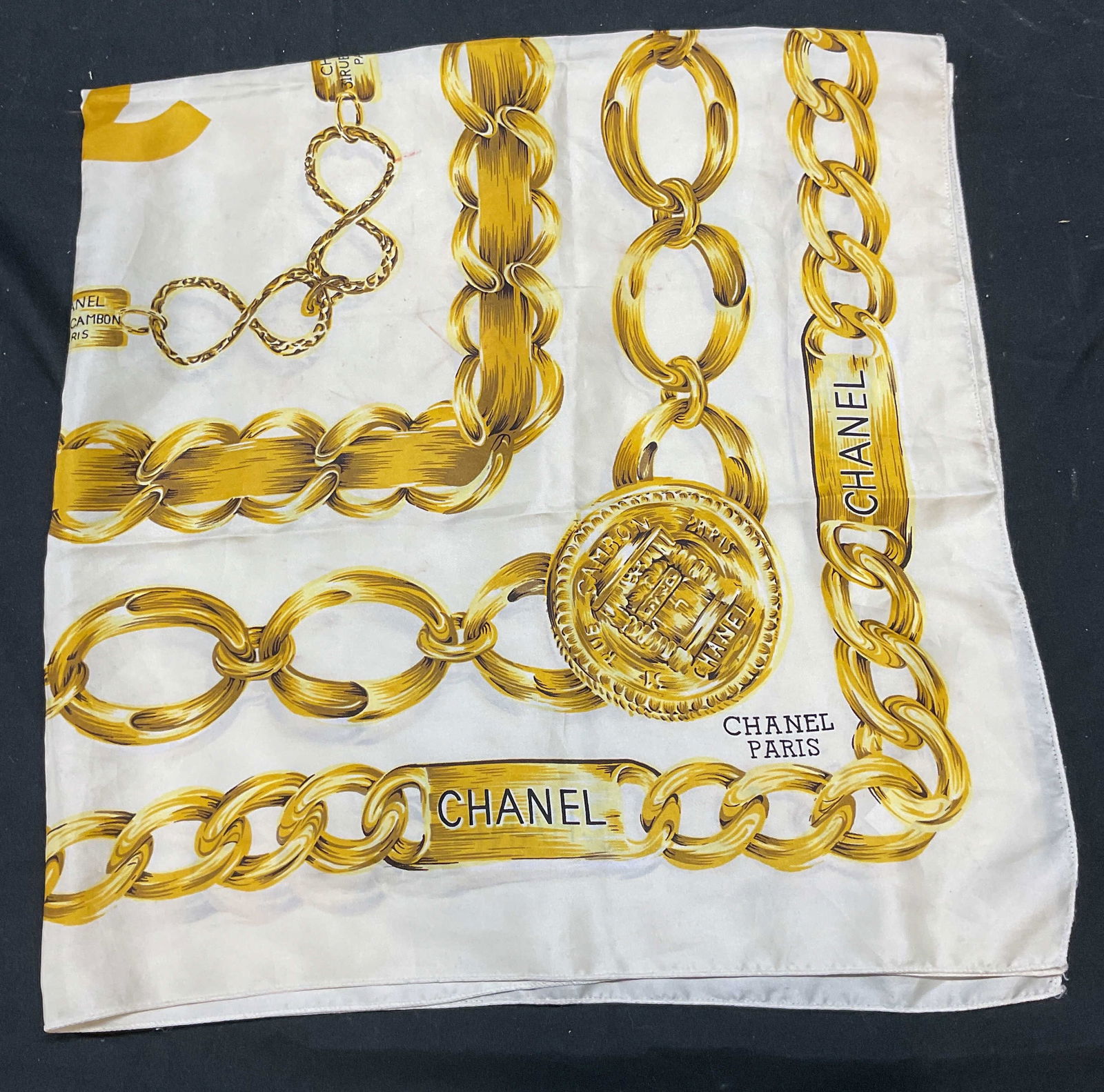 White & Gold Chain Print Silk Scarf: White and gold scarf with chain print. Feels like silk. Measures approx 34 x 34 inches. Some wear including pulling and blemishes observed. The Benefit Shop does not guarantee authenticity of any item