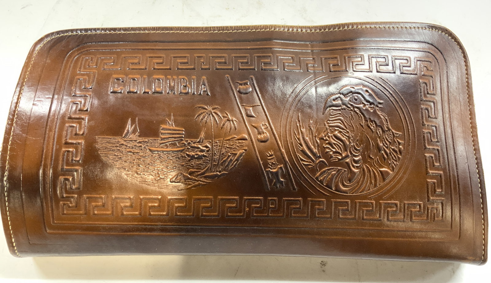 Embossed Zippered Leather Clutch COLOMBIA: Clutch reads COLOMBIA. Piece is light brown toned appears to be leather possibly leatherette. Clutch has embossed detailed with portrait image, geometric detail, & depiction of a boat at sea. Interior