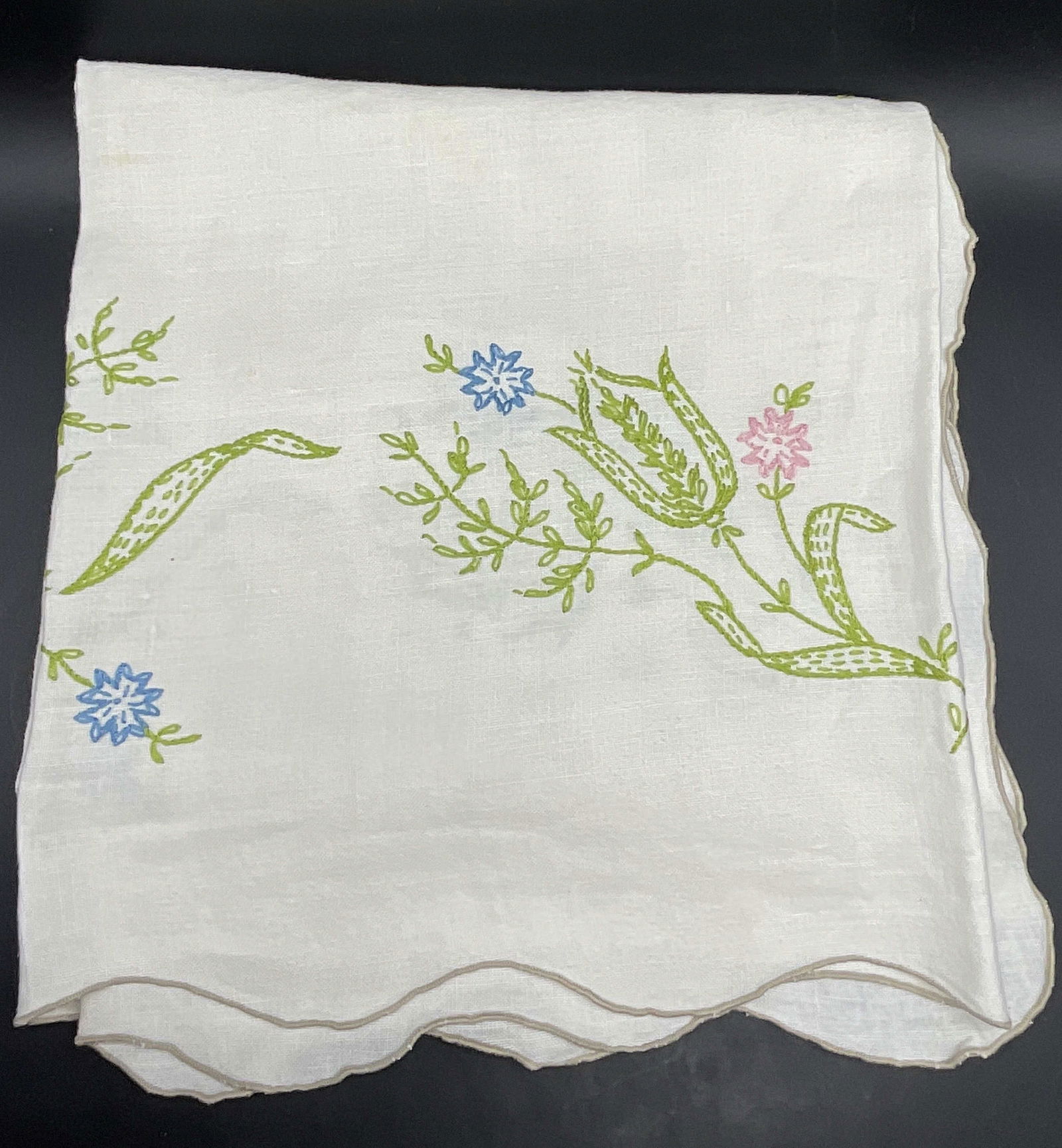 Vintage Embroidered Floral Motif Tablecloth: Vintage Embroidered Floral Motif Tablecloth. Crafted from soft hand fabric. White hued fabric decorated with green, pink, and blue floral embroidery. Measures approx. 48W x 48L in. Discoloration, resi
