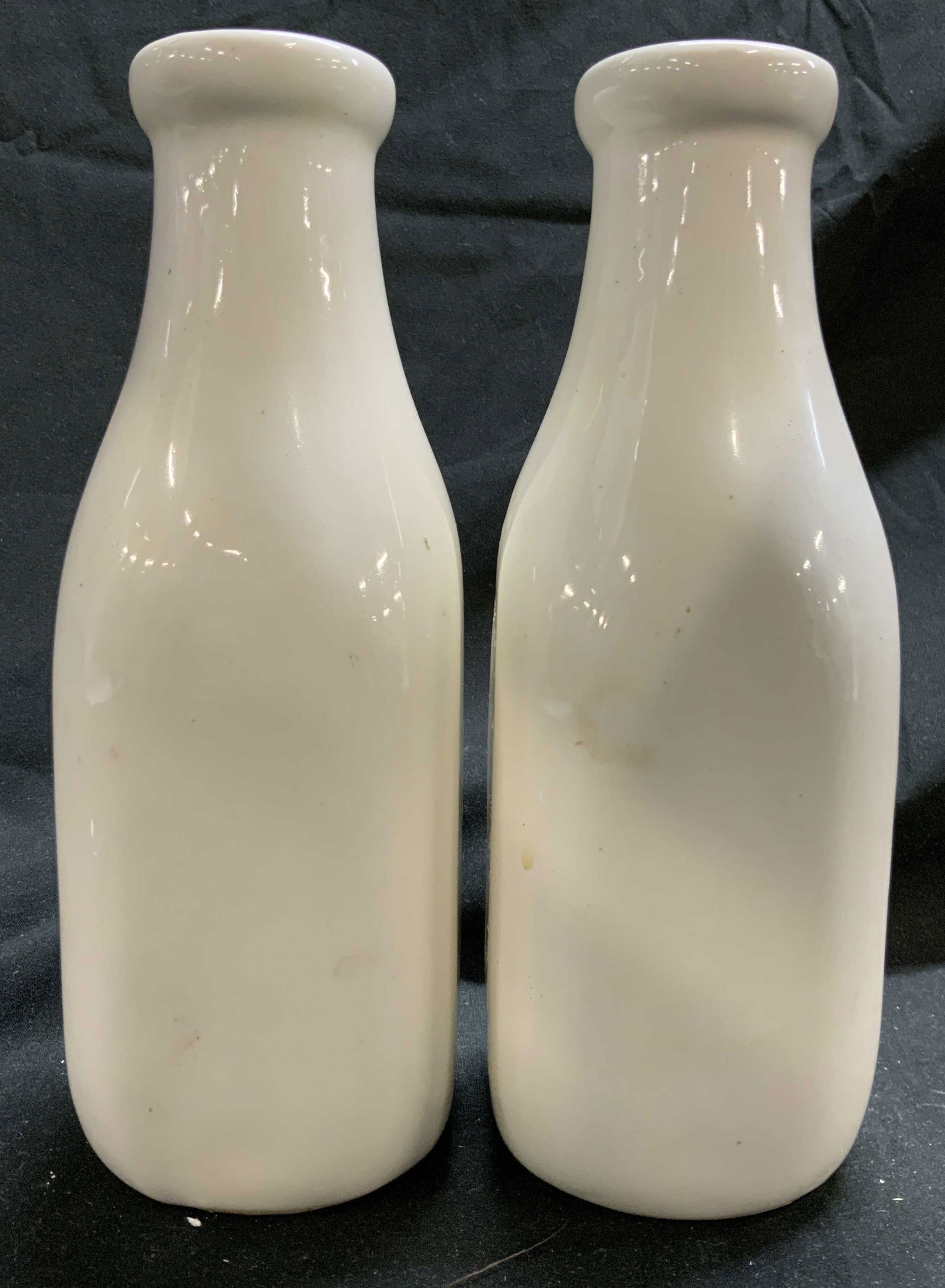 Pair Ceramic Porcelain Milk Bottles: Undersides are marked and trademarked illegibly, upcycle as vases. Lot includes 2 milk bottle. Each are white toned. Appears to be ceramic possibly porcelain. Outer rims are lipped. Each measures appr