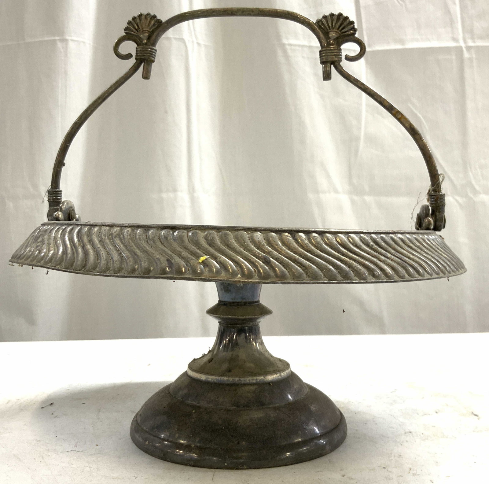 Quad Plated MERIDEN B CO Pedestal Bride Basket: Underside is inscribed QUADRUPLE PLATED MERIDEN B COMPANY. Bride basket is vintage. Piece has handle with curled structures. Rim exterior is Scalloped. Base of pedestaled area has circular form. Piece