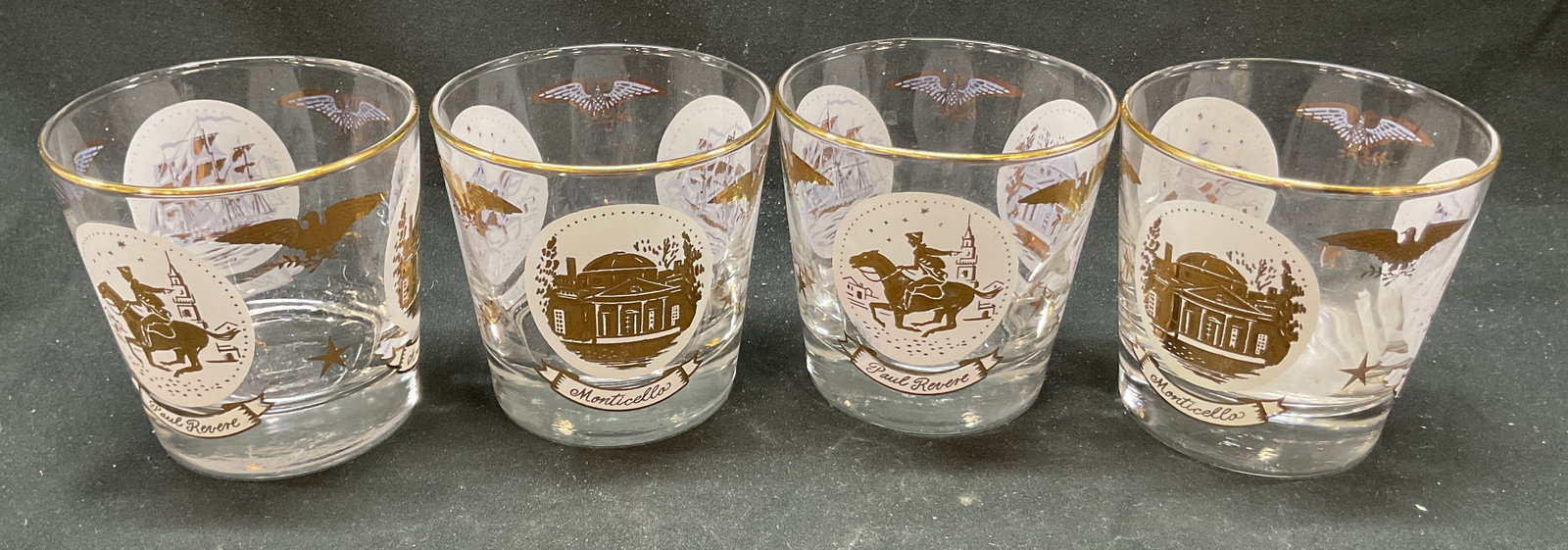 Set 4 Vtg Libbey Americana Patriotic Glasses: Set 4 vintage Libbey Americana patriotic glasses. Gold plated rims and designs. Old fashioned Barware whiskey glasses. Includes text saying Paul Revere, Monticello, Old Ironsides. 3.5 x 3.24 inches. S