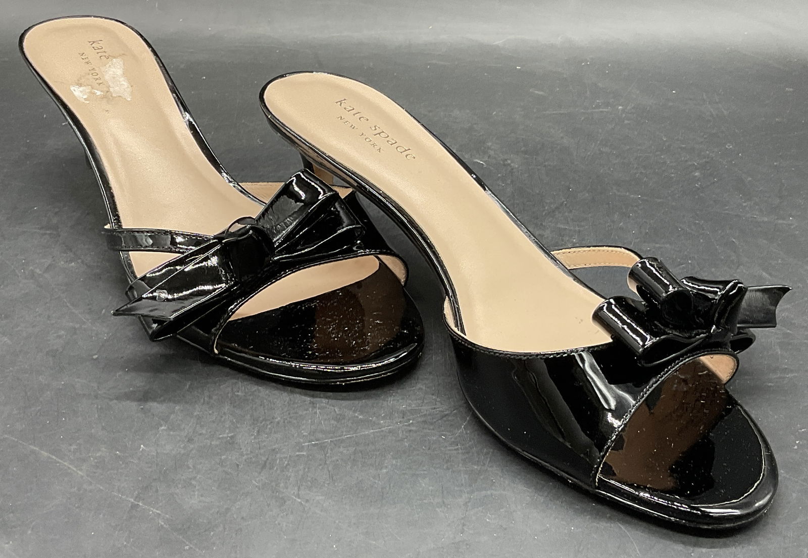 KATE SPADE NEW YORK Black Bow Motif Heels: KATE SPADE Black Ribbon / Bow Accent Heels. Underside reads KATE SPADE 7 1/2. Length measures approx. 10 inches. Crafted from patent leather or leather style materials. Surface wear consistent with ag