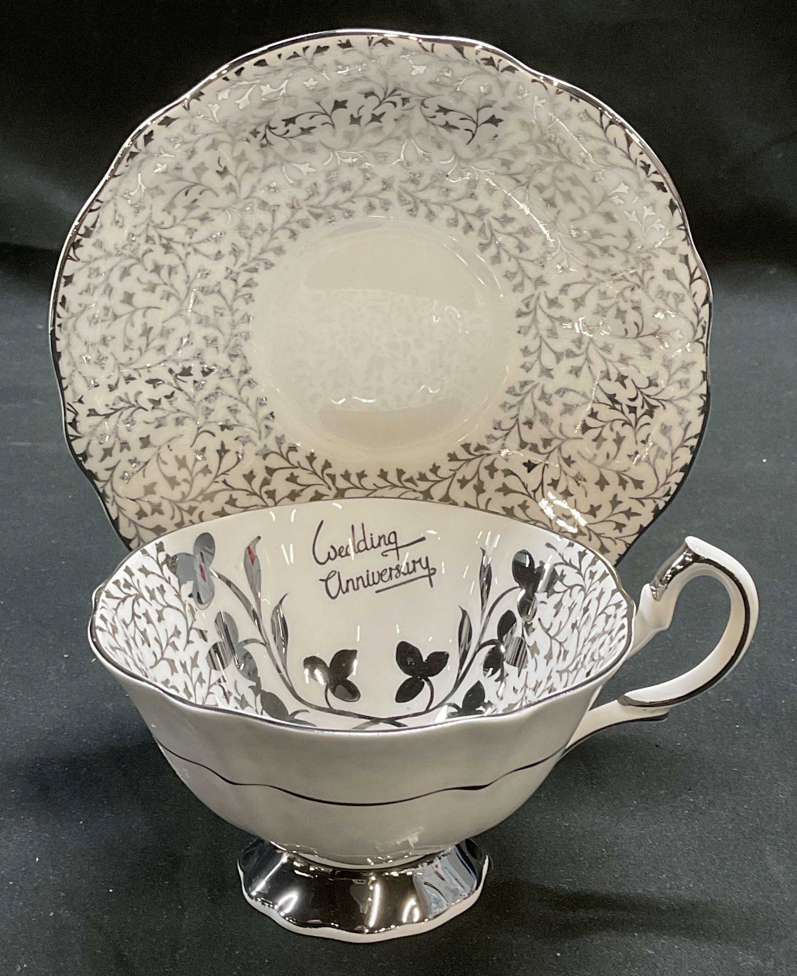 Queen Anne China Teacup & Saucer, England: Queen Anne bone china teacup in saucer with silver scroll pattern. Wedding anniversary. Signed. Saucer approx 5.5 inches, teacup approx 4 x 2.5 inches. Some wear to each including scratching. Queen An