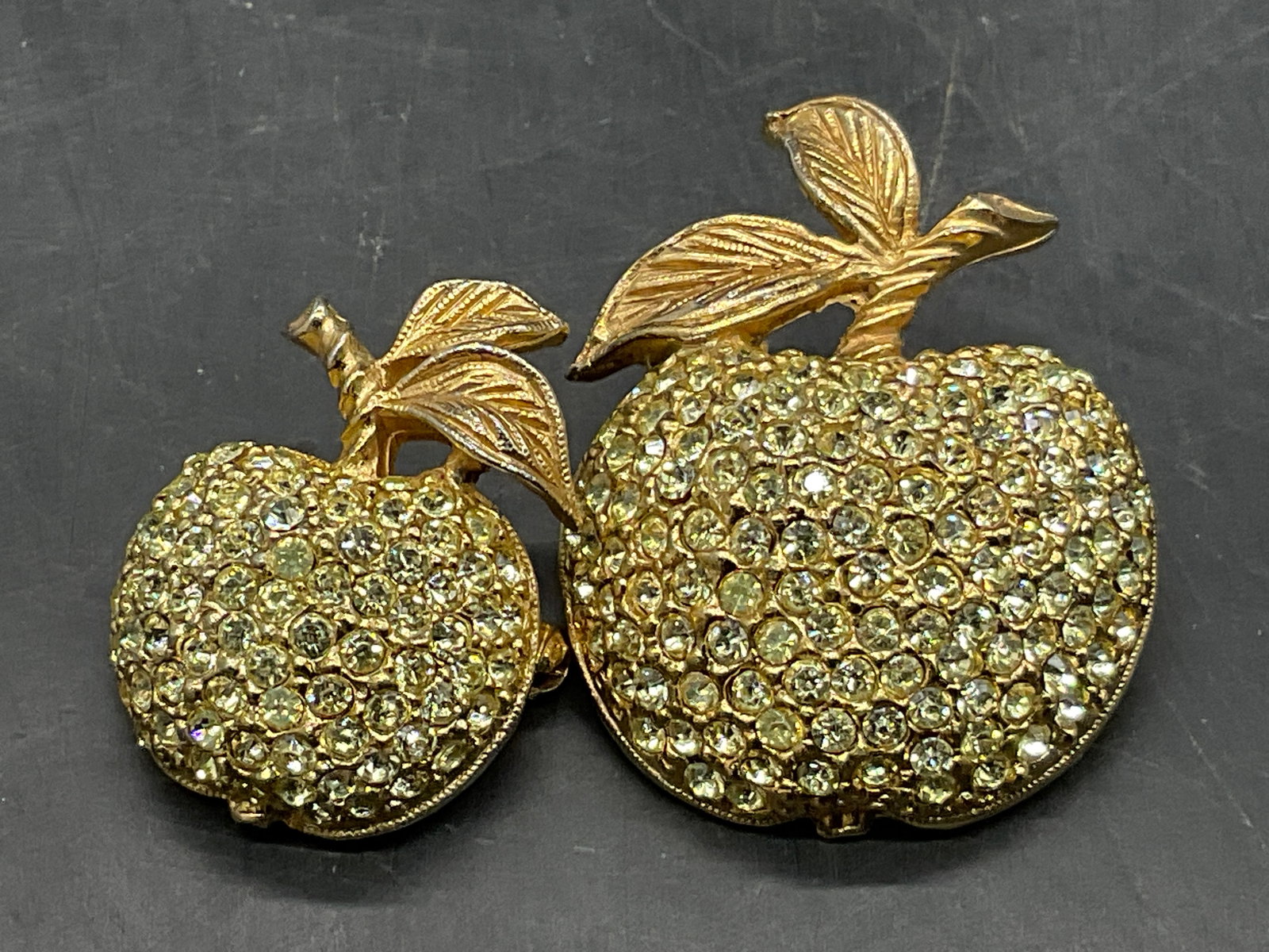 Lot 2 Vintage Bejeweled Crystal Apple Brooches: Two Vintage Bejeweled Crystal Apple Brooches. Studded with faceted crystals. Metal pin closures to reverse. Larger apple measures approx. 1.5L x 1W in. Discoloration, surface wear, and residue present