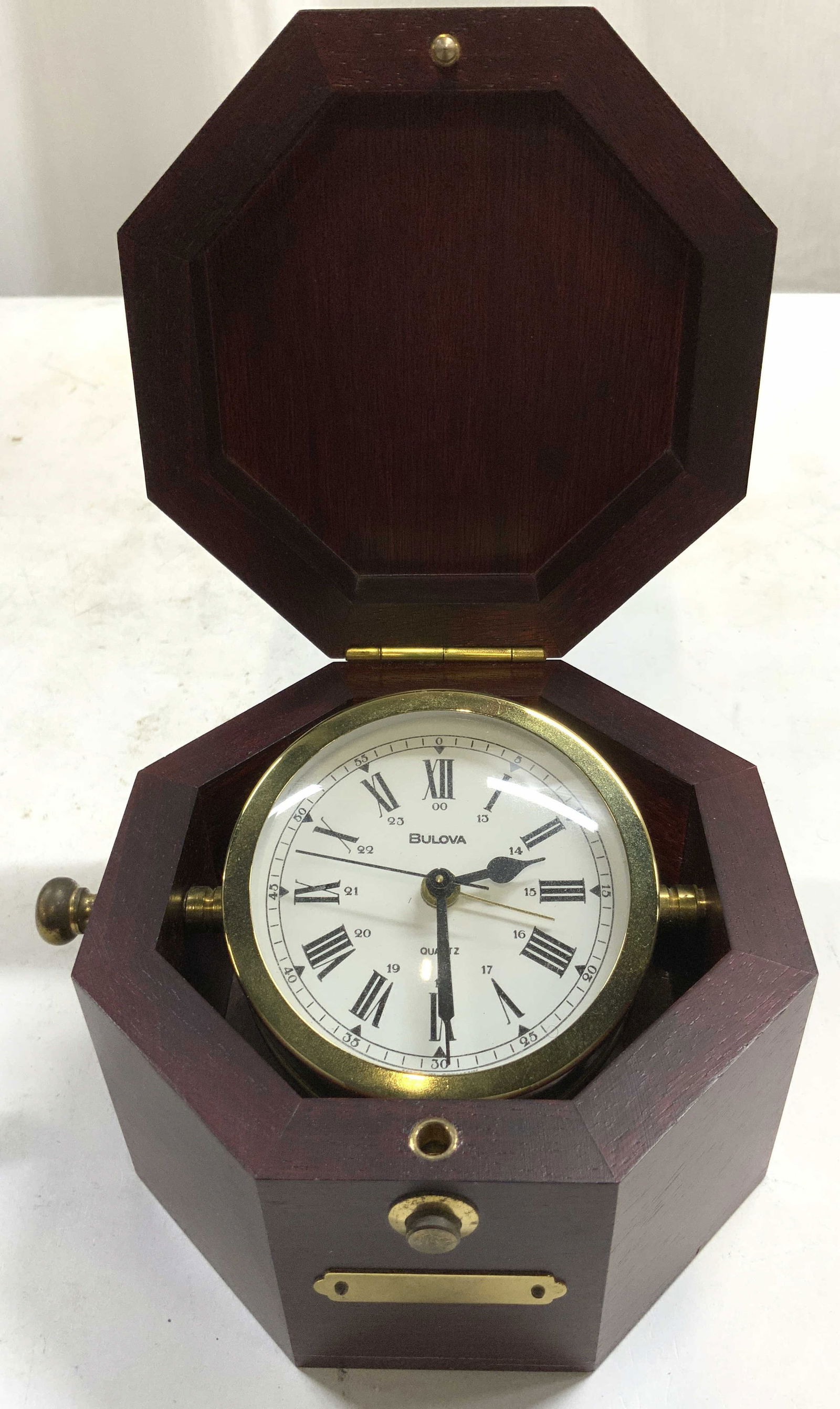 BULOVA Quartermaster Maritime Clk W Lid Germany: Clock face reads BULOVA. Clock has white face with black toned Roman numerals and hands. Clock edge is gilt metal. Clock sits in mahogany toned octagonal box with lid. Underside inscribed MADE IN GERM