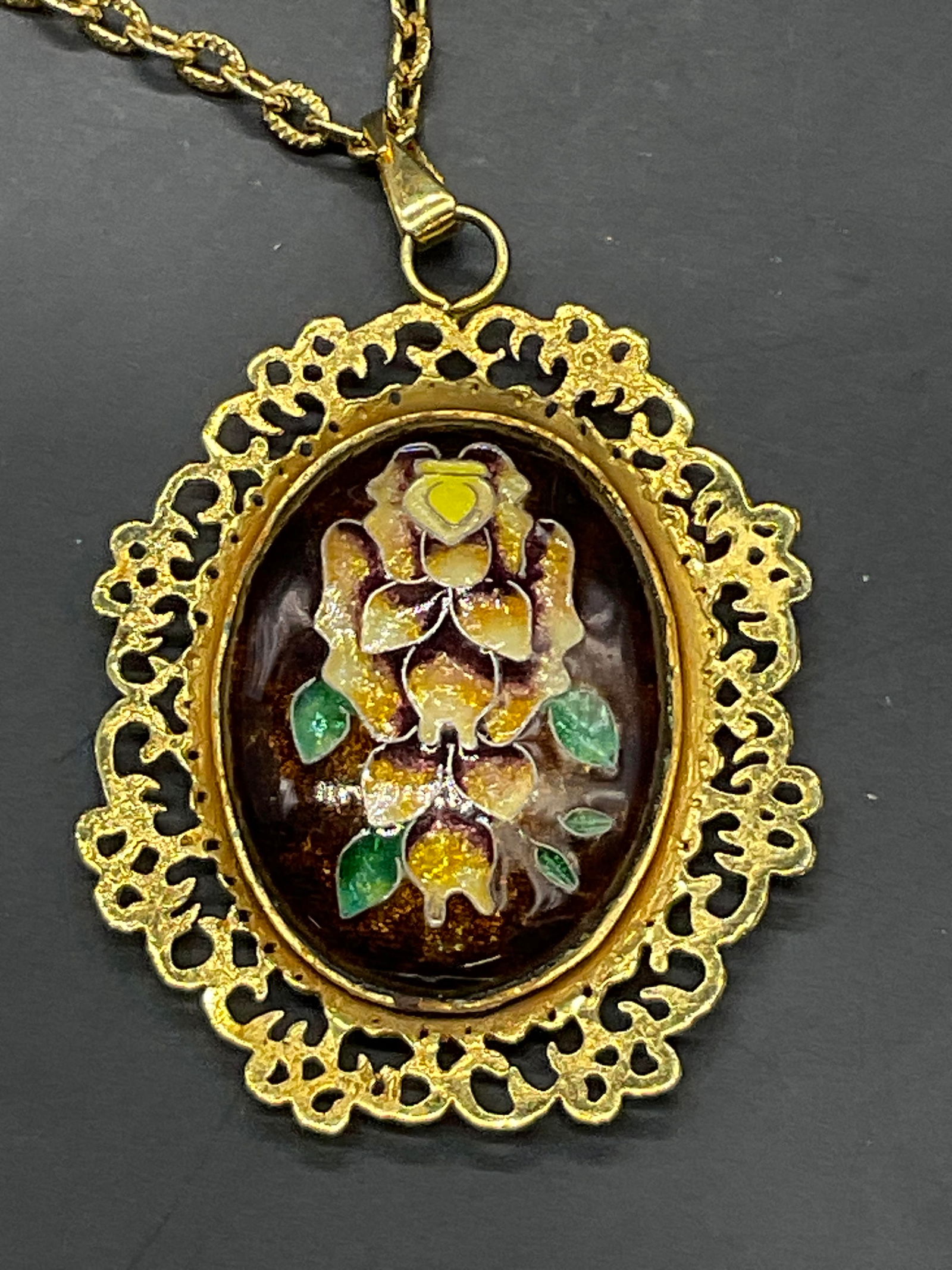 HONEY CLOISONNE Floral Pendant Necklace: HONEY CLOISONNE Floral Pendant Necklace. The pendant features brown, green, yellow, and purple hues. The backing to the pendant reads HONEY CLOISONNE. Necklace chain length measured end to end approx.