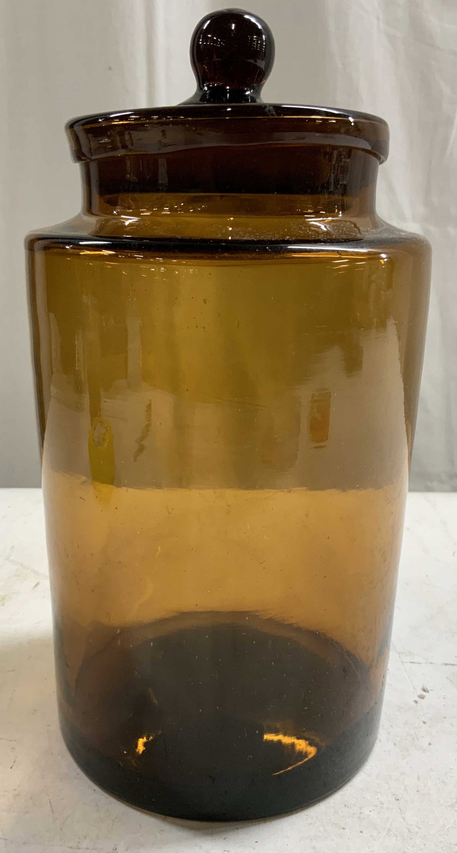 Vintage Amber Glass Apothecary Jar W Lid: Apothecary jar is amber toned. Piece includes lid with knob style handle. Jar appears to be vintage. Amber glass jar with lid. Piece measures approximately 10 inches tall 5.5 inches wide. Jar, apothec