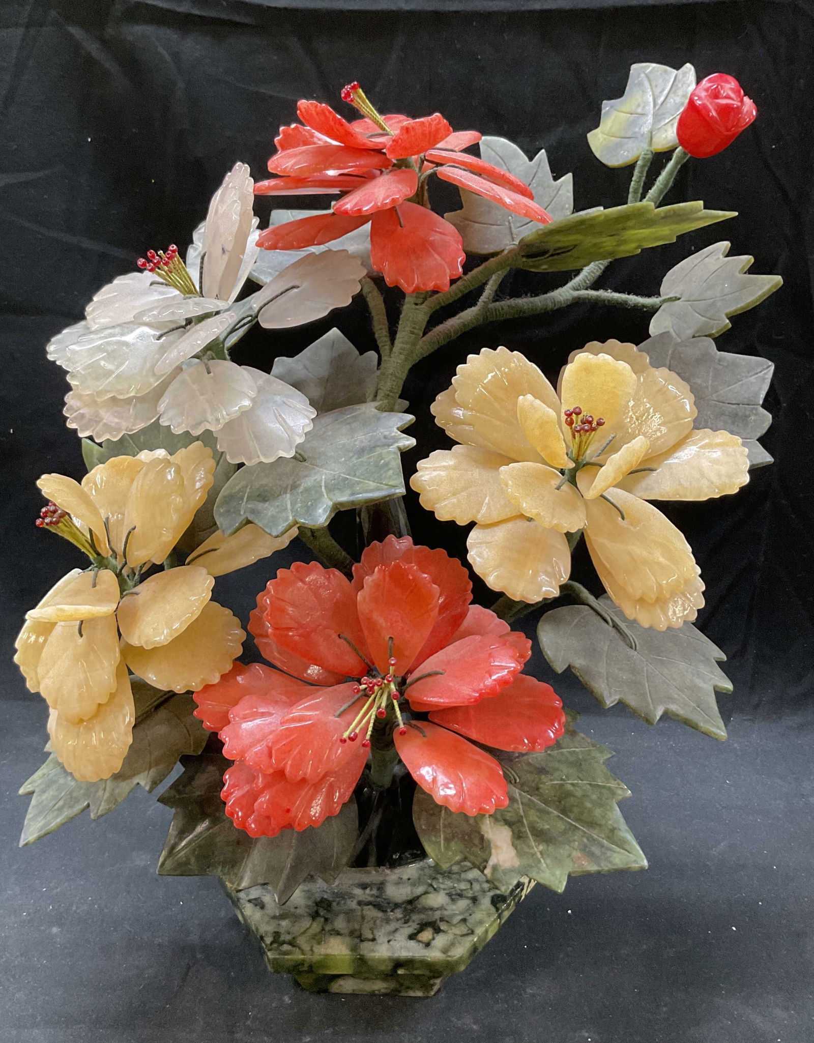 Vtg Hand Carved Jade Floral Sculpture: Vintage hand carved jade floral sculpture. 5 flowers in orange pink, yellow, white colors and leaves. Material appears to be jade or similar semi precious stone 16 x 12 x 7 inches. Some surface wear c