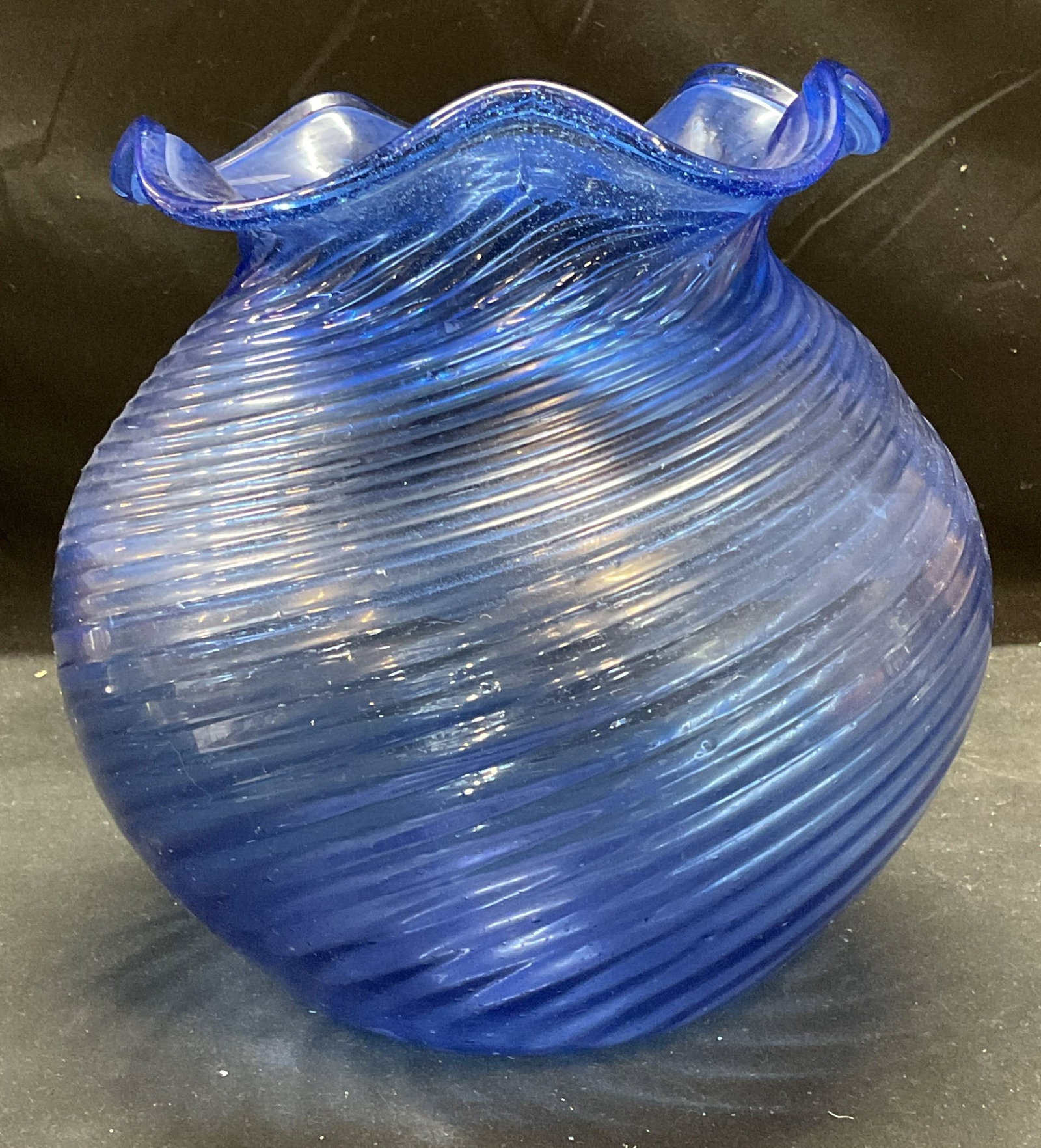 Hand Blown Blue Art Glass Ribbed Ruffle Vase: Hand blown art glass vase in blue. Rounded shape with raised swirled ribbed design and handkerchief ruffle rim. Measures approx 8 x 8.75 inches. Some scratching observed. Art glass vase, blue vase, sw