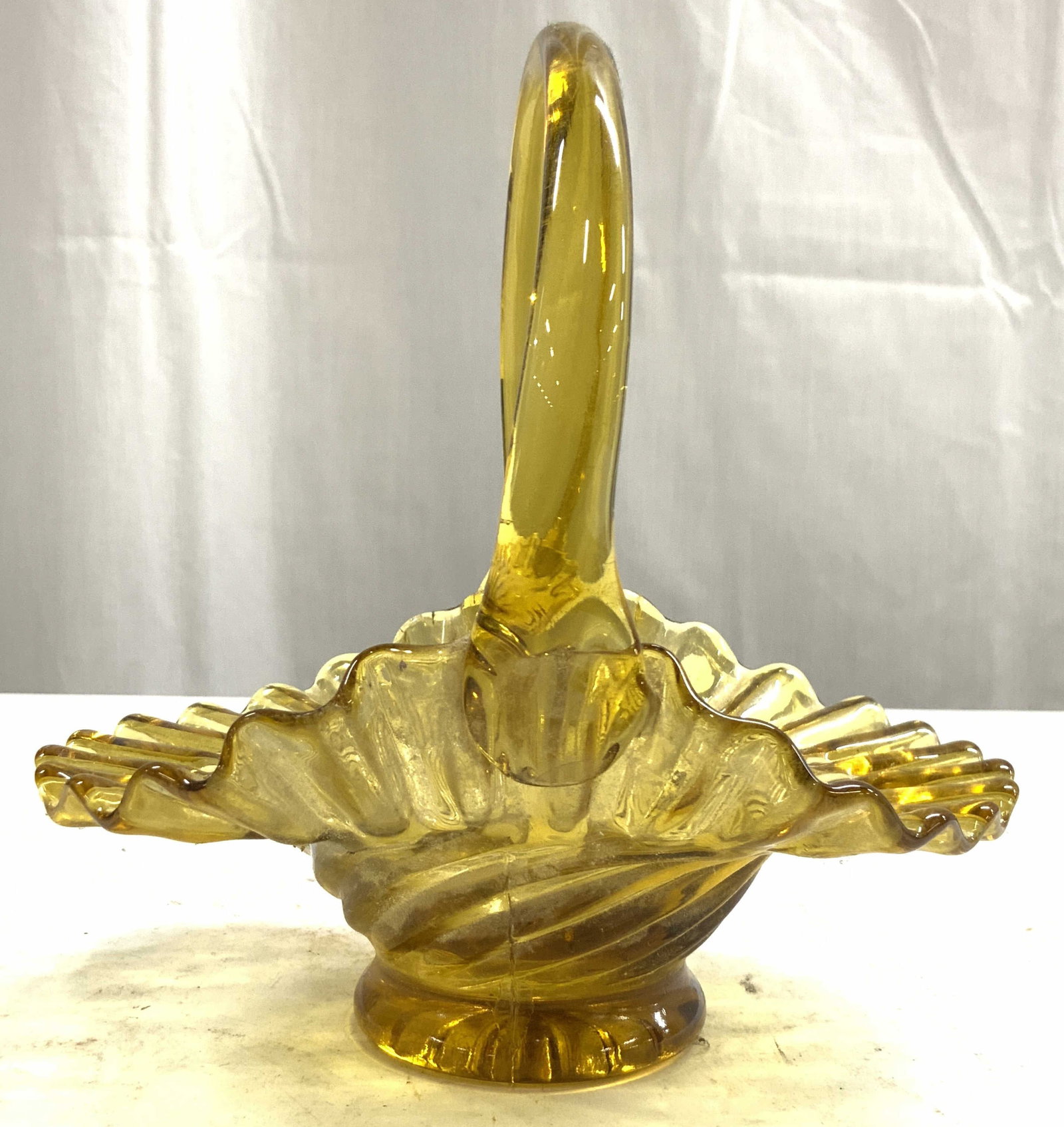 Vntg Handkerchief Style Amber Glass Basket: Basket is vintage. Piece has handkerchief style form with fills and folds. Basket has arch form handle. Vessel is amber toned. Piece is glass. Measures approximately 6.5 inches tall and deep 5 inches 