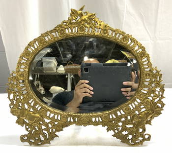 Vtg Victorian Ornate Standing Brs Tbltop Mirror: Mirror is gold toned and brass. Piece is vintage. Mirror has beveled surface with oval form. Vintage Victorian mirror with ornate scroll, floral, leaf and cherub detail. Top of piece has hummingbird d
