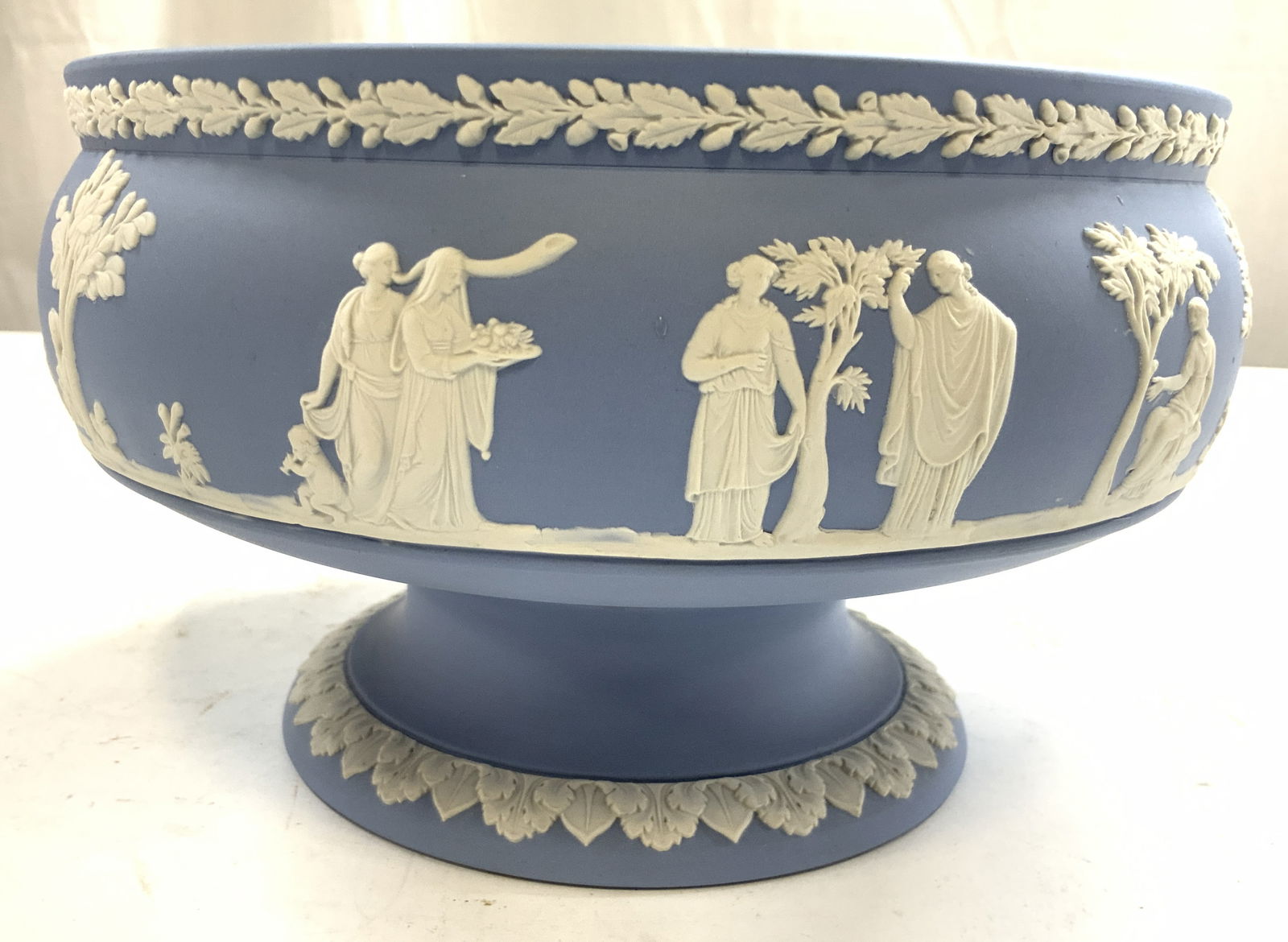 WEDGWOOD Pedestaled Blue Jasperware Bwl ENGLAND: Underside is inscribed WEDGWOOD MADE IN ENGLAND. Bowl is pedestaled. Piece is Vintage. Bowl is light blue toned with white female figure, cherubs, tree and leaf detail. Bowl measures approximately 9 i