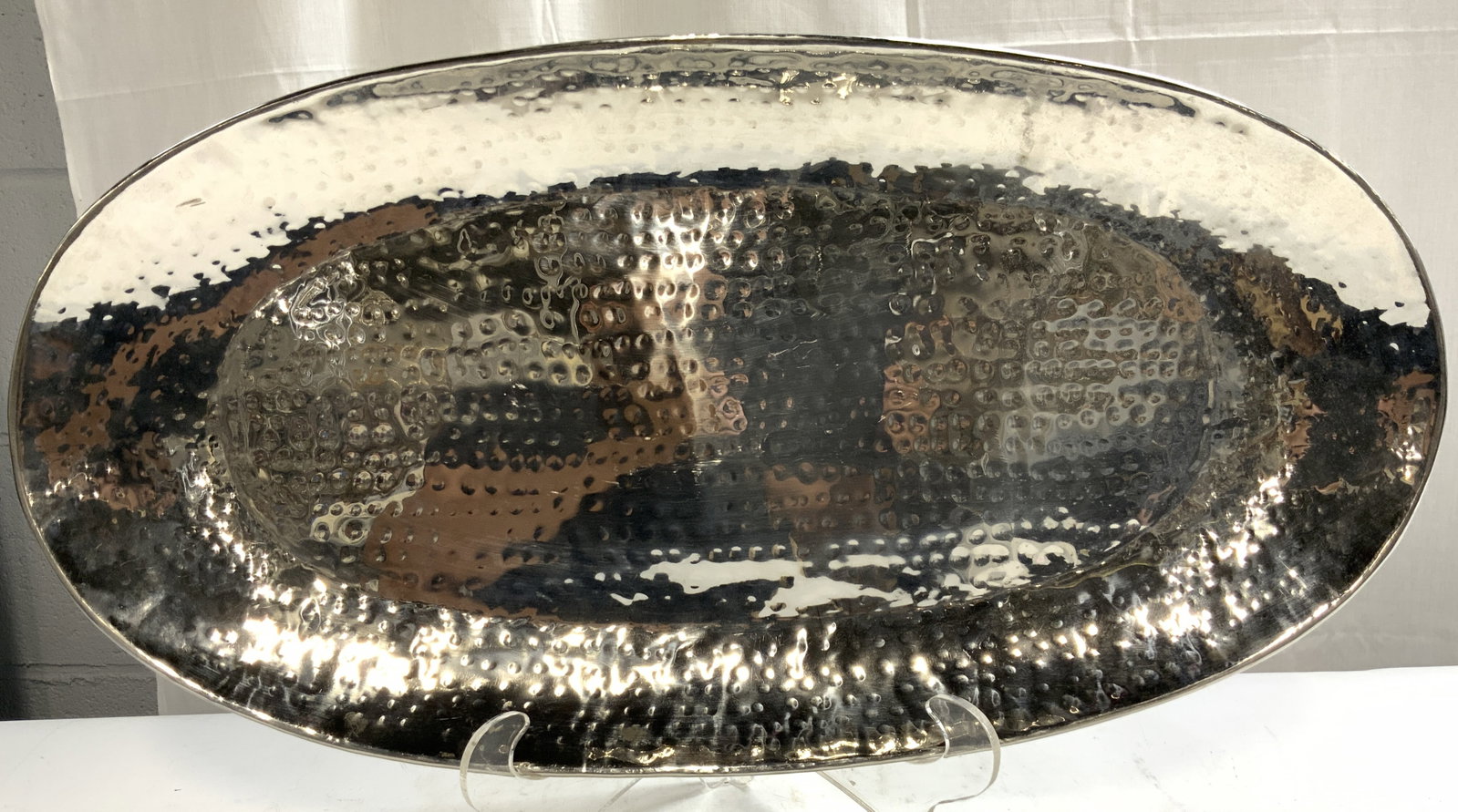 TOZAI Oval Hammered Metal Centerpiece Tray 27in: Tag on underside reads TOZAI. Tray is silver toned hammered metal. Outer rim is lipped. Piece has dimples throughout structure. Tray has oval form. Piece measures approximately 27 inches ling 14 inche