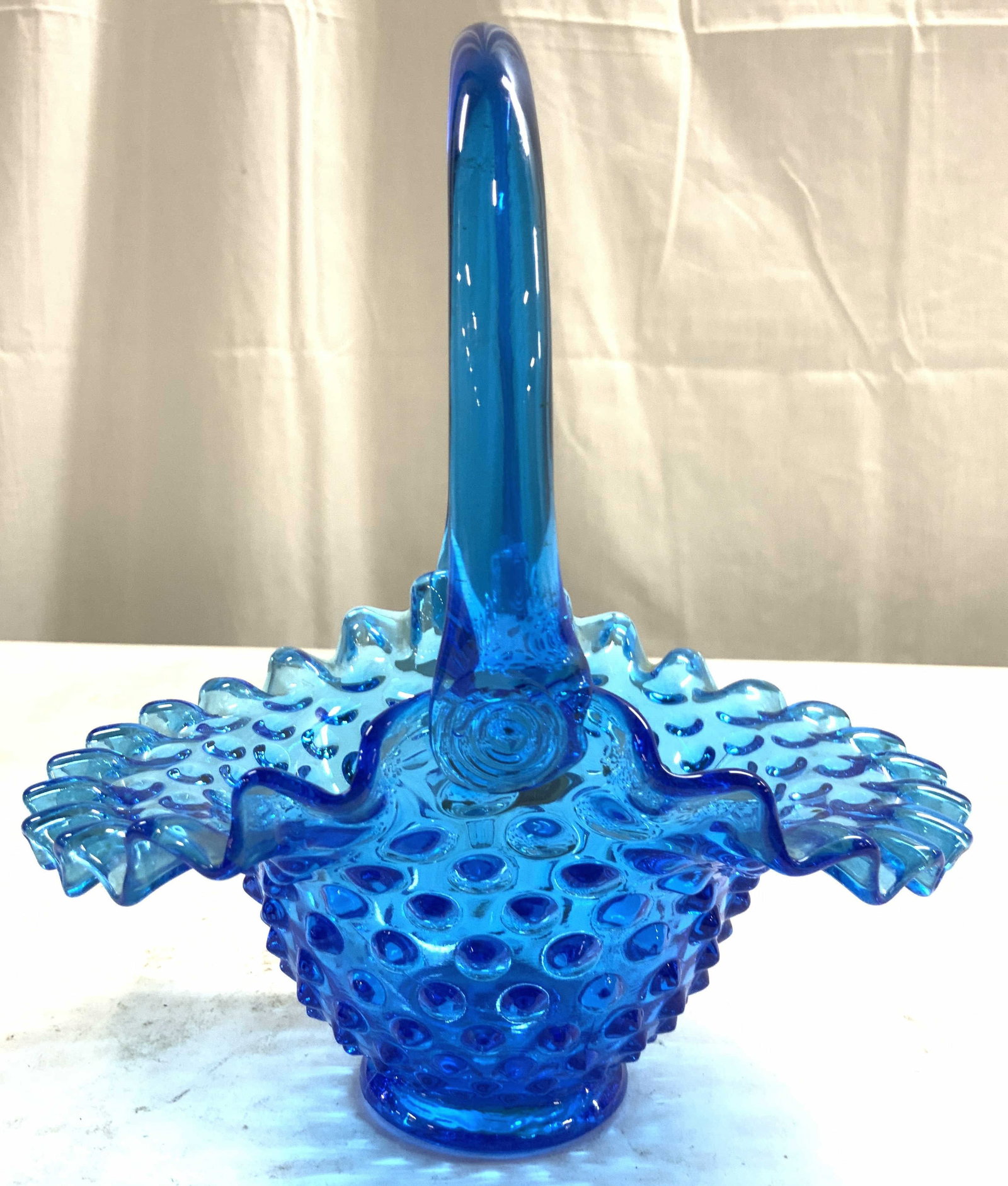 Fenton Vtg Colonial Blue Hobnail Glass Basket: Tag reads FENTON HANDMADE. Colonial blue art glass basket with frilled rim. Basket has arch form handle. Hobnail basket with studded exterior. Piece measures approximately 8 inches tall 7 inches deep 