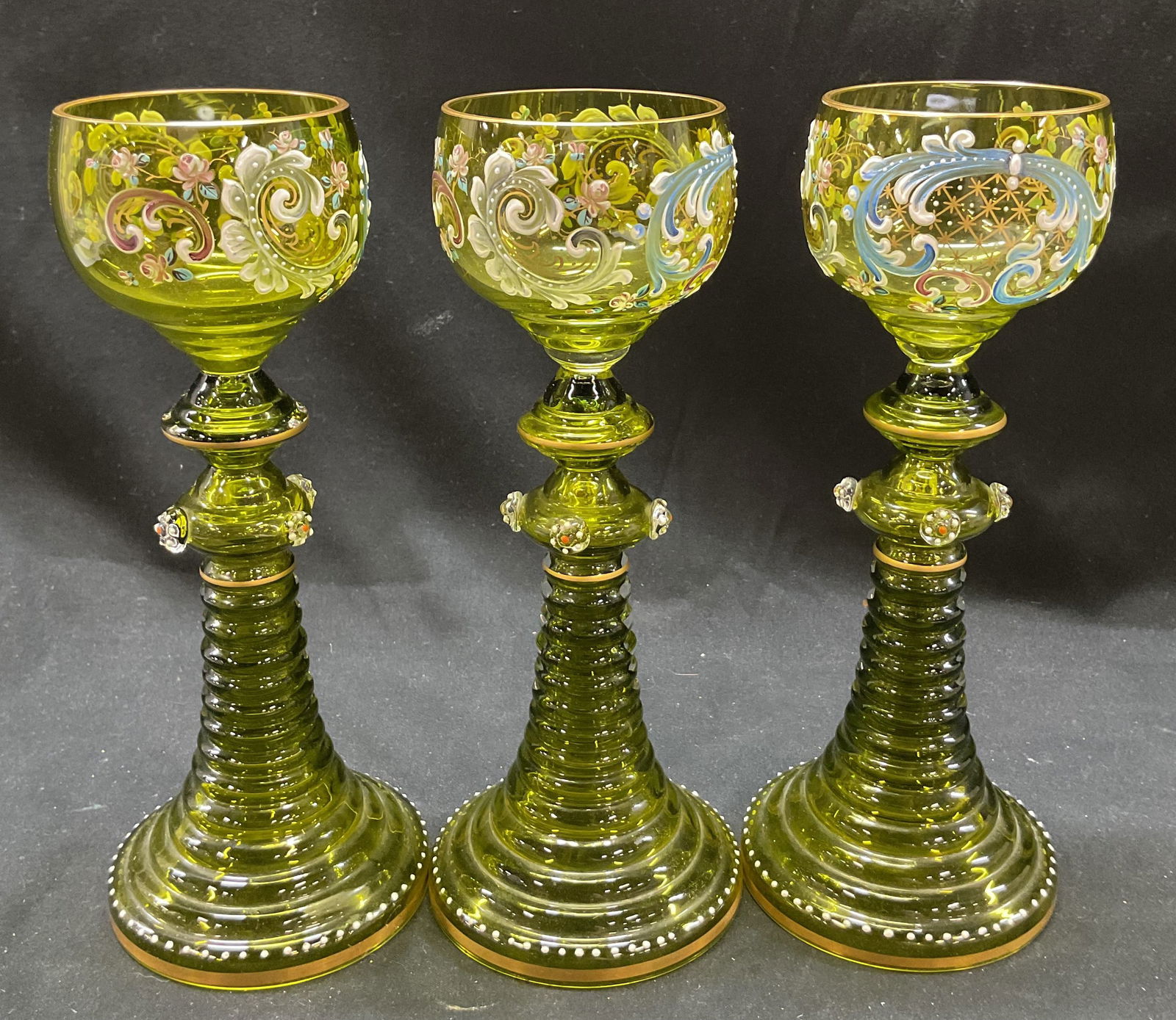 Set 3 Moser Green Glass Floral Wine Goblets: Set 3 moser green glass floral wine goblets. Gilded floral pattern designs, cordial glass. Cordial glass with gilded borders on top and bottom. Ribbed trumpet base. 8 x 3.5 inches. Some surface wear c