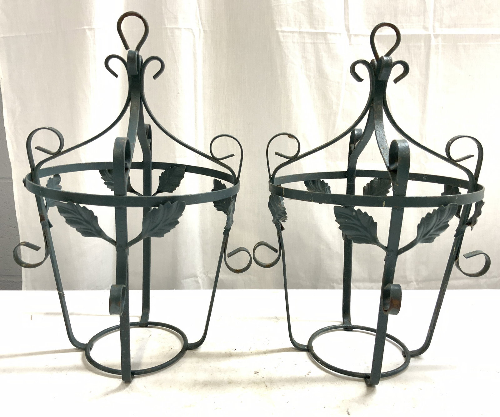 Pr Vntg Iron Hanging Planter Holders: Lot includes 2 planter holders. Each are green toned and metal, appear to be iron. Each have leaf and s curl detail. Tops of each piece have loops for hanging. Each piece measures approximately 14.5 i