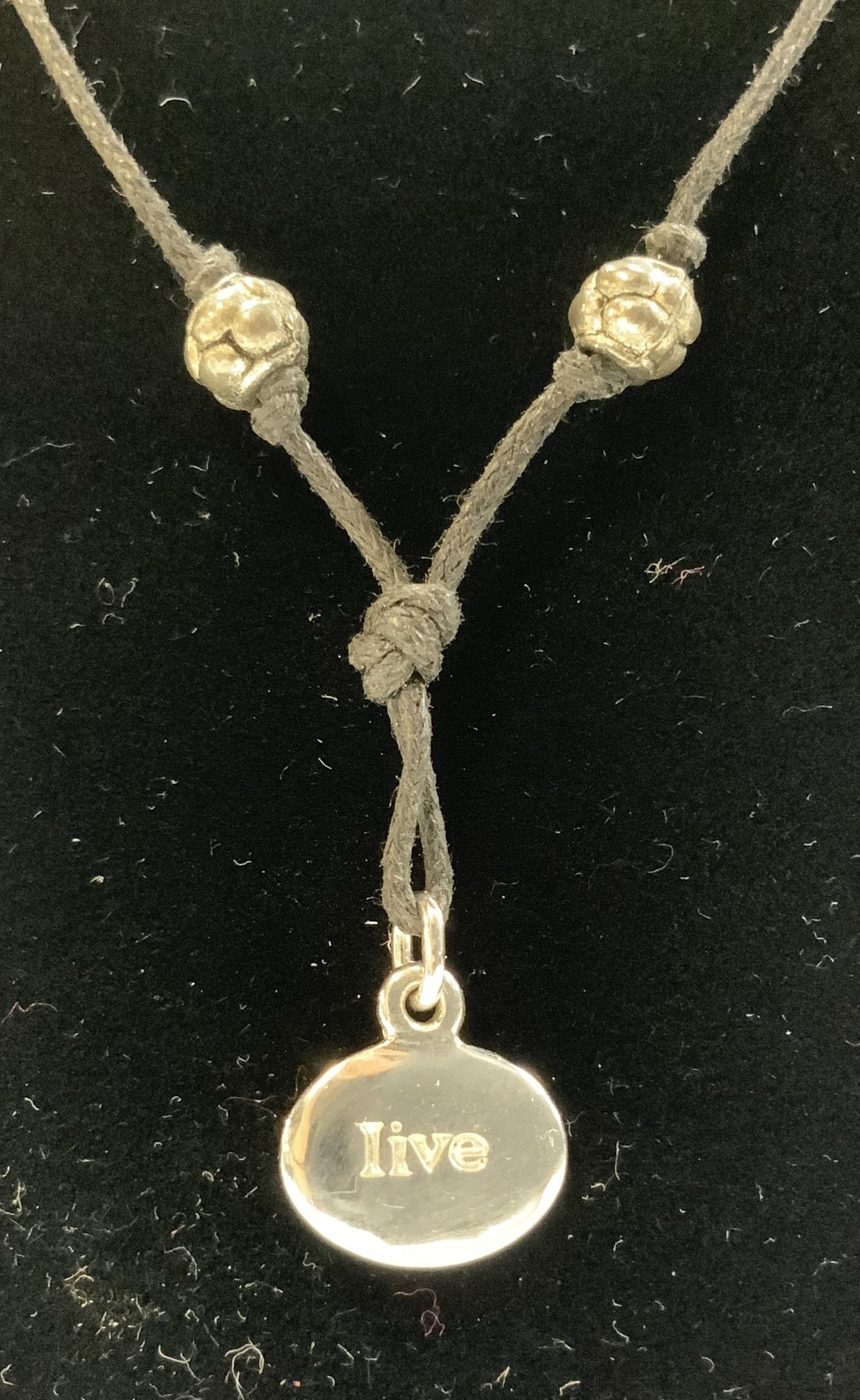 LIVE 4 LIFE Adjustable Silver-Toned Necklace: LIVE 4 LIFE Adjustable Silver-Toned Necklace Necklace features an adjustable black cord with decorative beads. A circular silver-toned pendant inscribed with the word LIVE & LIVE 4 LIFE, EMMA & ME. Su