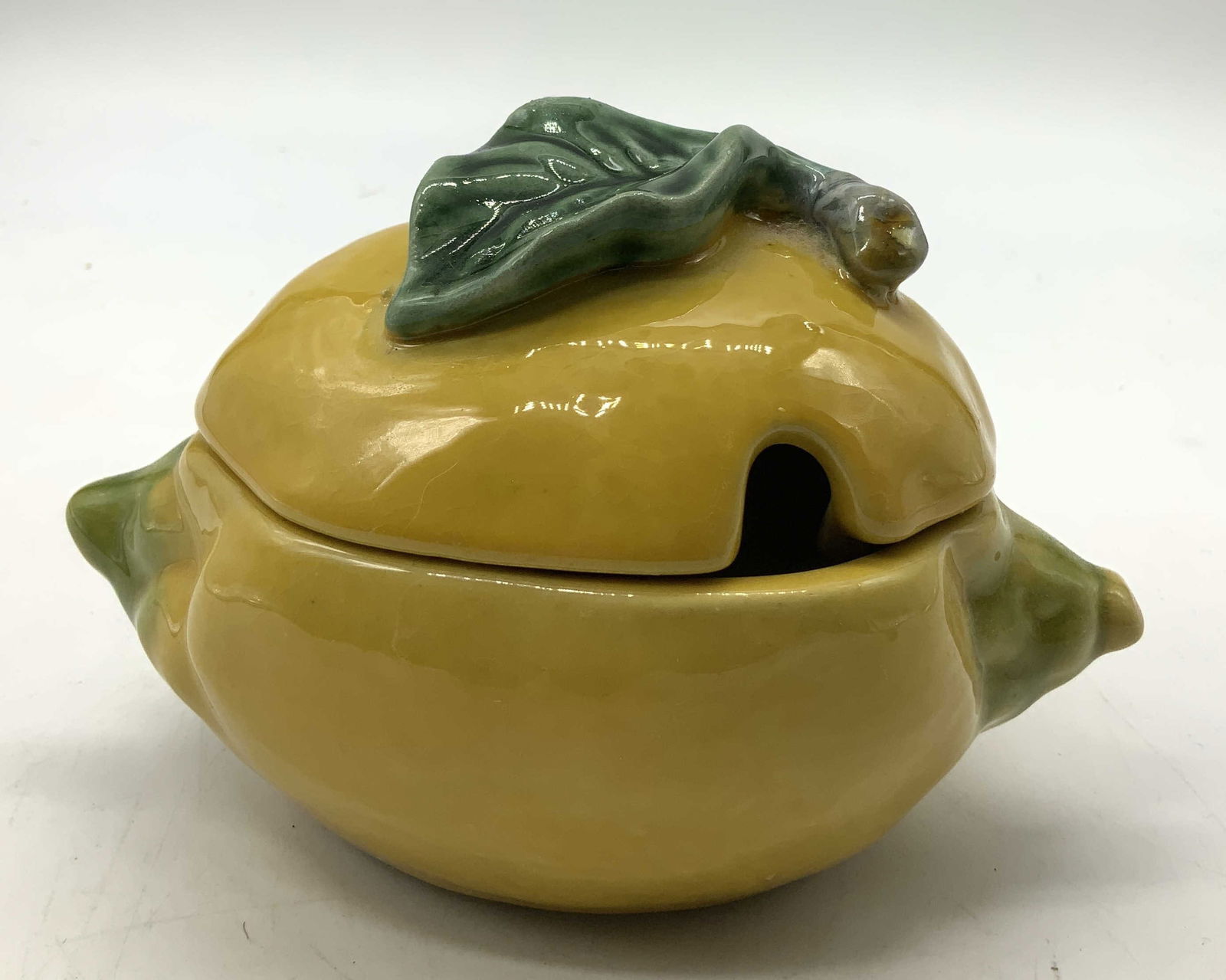 Vintage Majolica Lemon Lidded Condiment Dish: Condiment dish features a vibrant yellow glaze & a green leaf lid. Lid features a notch, used for a spoon. Surface wear consistent to age, use & exposure. Measurements: length 5.7in x width 3.2in x he
