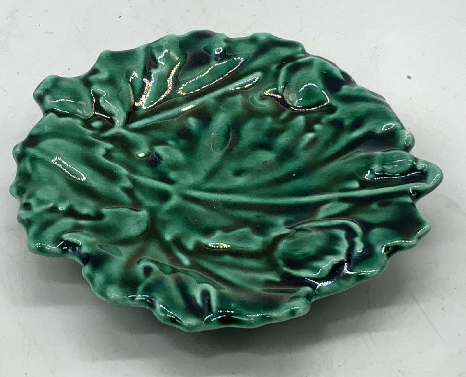 Vntg Majolica Raised Relief Leaf Trinket Dish: Vntg Majolica Raised Relief Leaf Trinket Dish Trinket dish features a raised relief design. Dish has a green glossy finish & scalloped edge. Surface wear consistent to age, use & exposure. Measurement